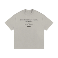 T-shirt by Wolvyn Apparel, front view, light gray cotton with black slogan Some brands follow culture. We build it.