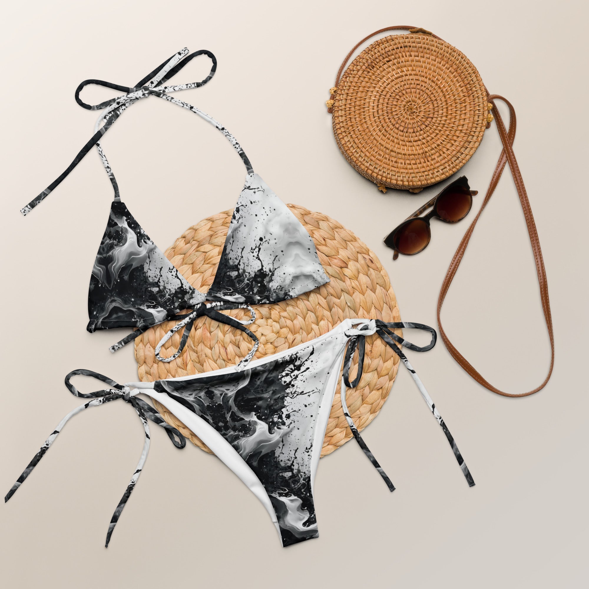 Black and white marble print string bikini set with straw bag and sunglasses on neutral background