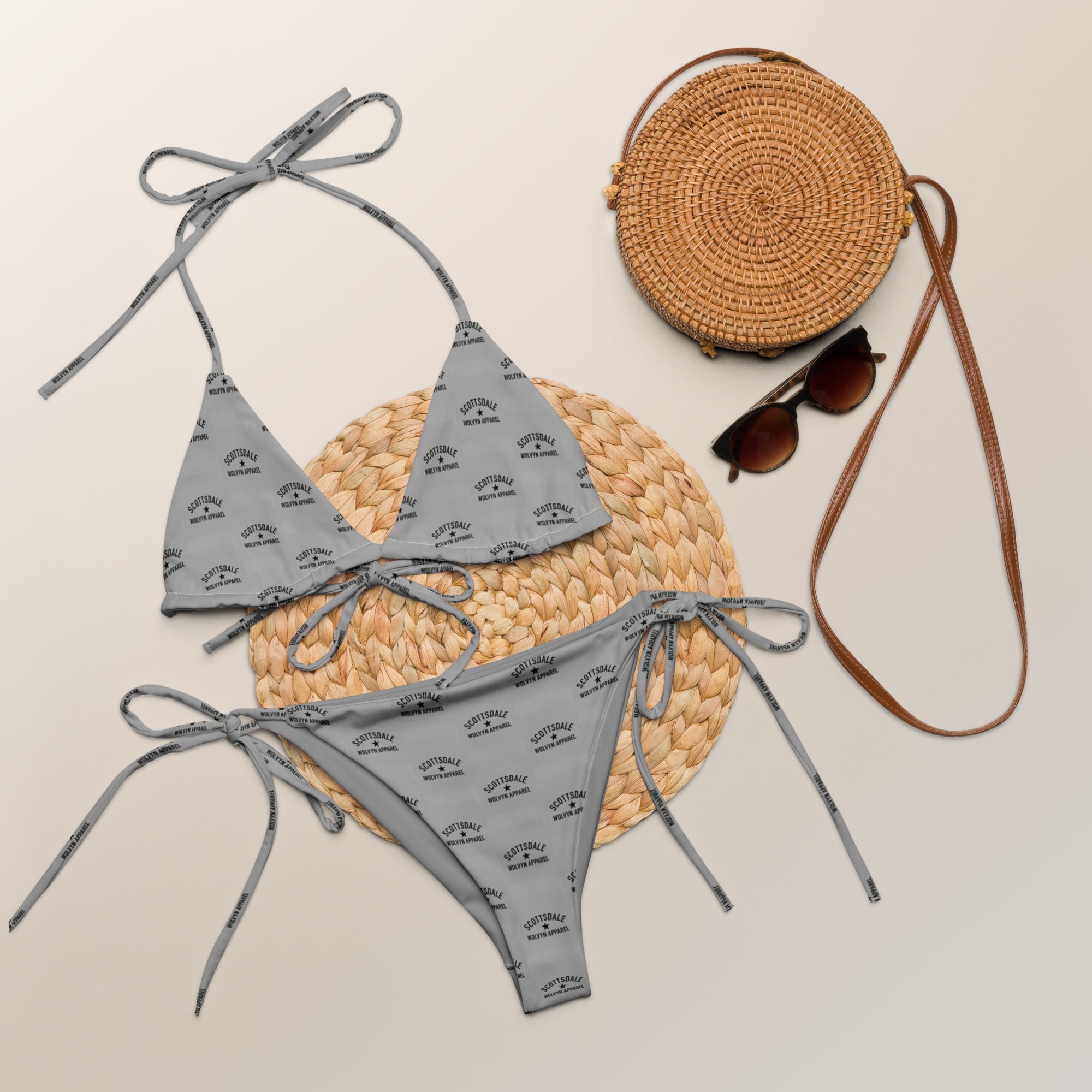 Gray string bikini with black text print displayed with woven bag and sunglasses on neutral background