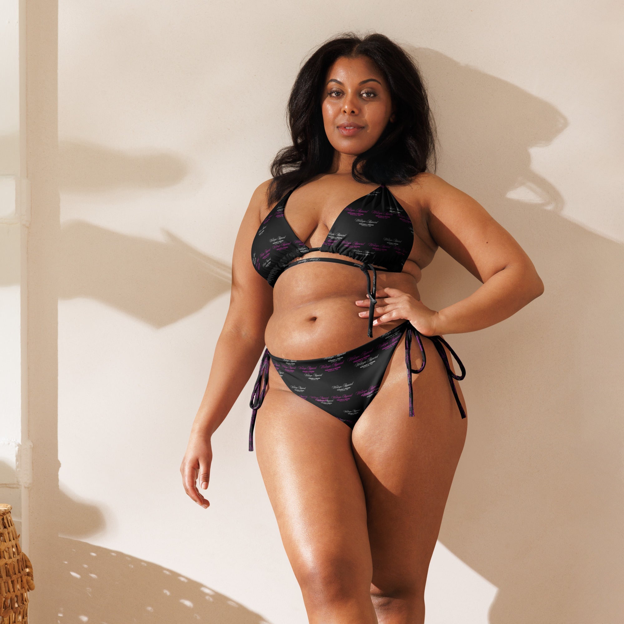 Woman modeling black all-over print recycled string bikini with side ties, indoor setting