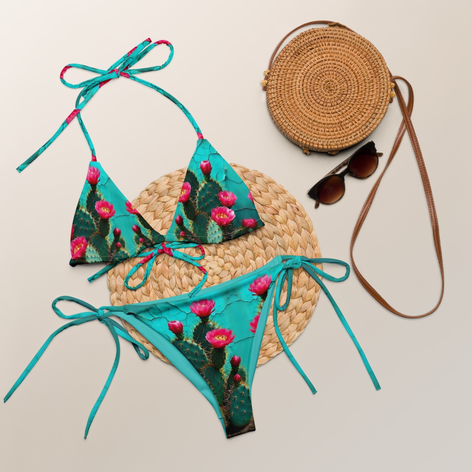 Turquoise cactus print string bikini set with woven straw bag and sunglasses on neutral background