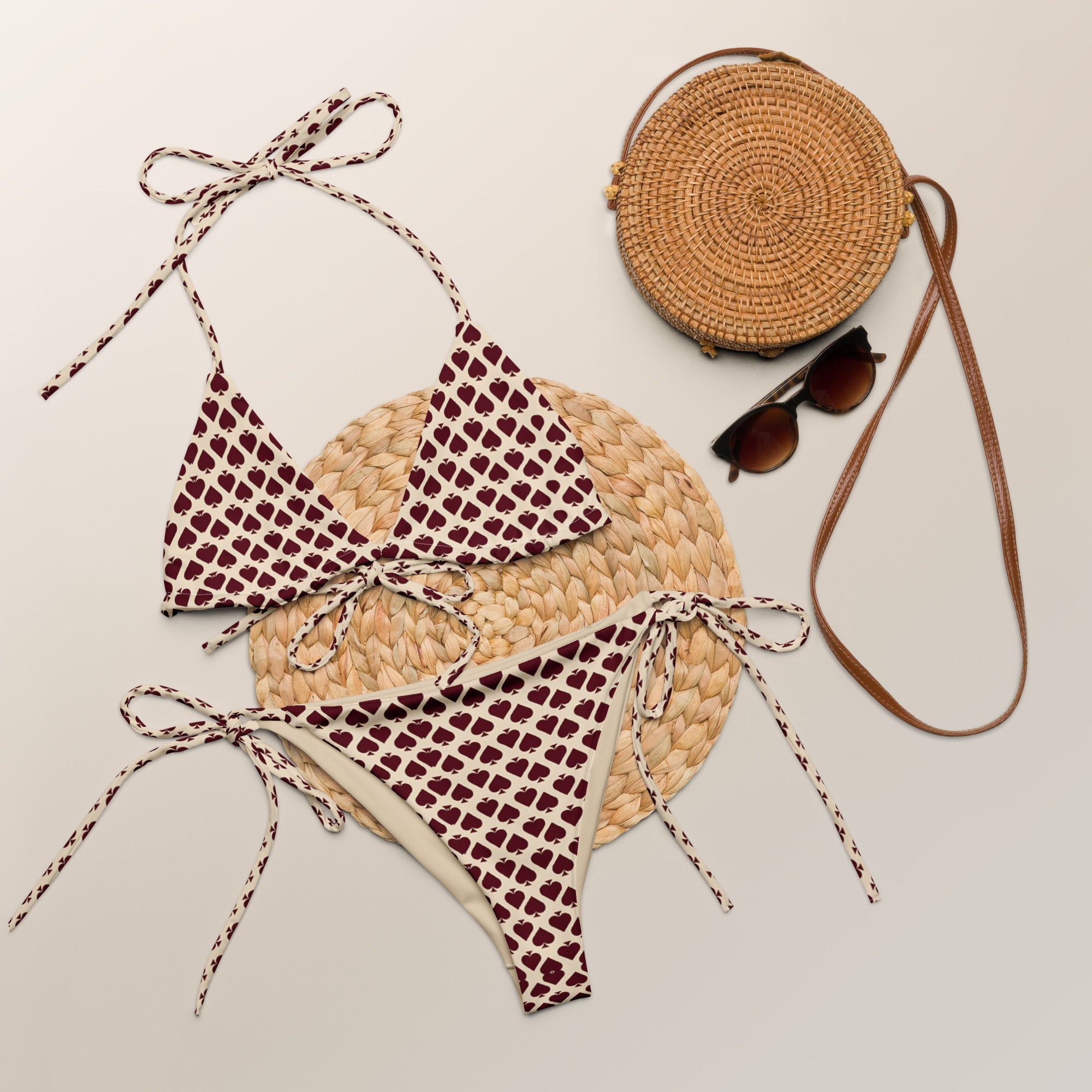 All-over print string bikini with maroon apple pattern, styled with rattan bag and sunglasses.