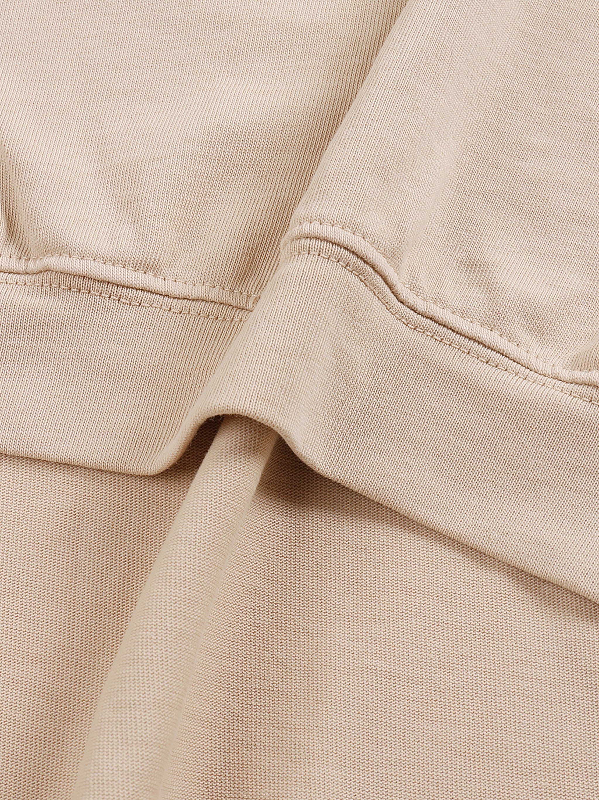 Close-up of beige heavyweight cotton fabric with asymmetric seam detailing on a t-shirt