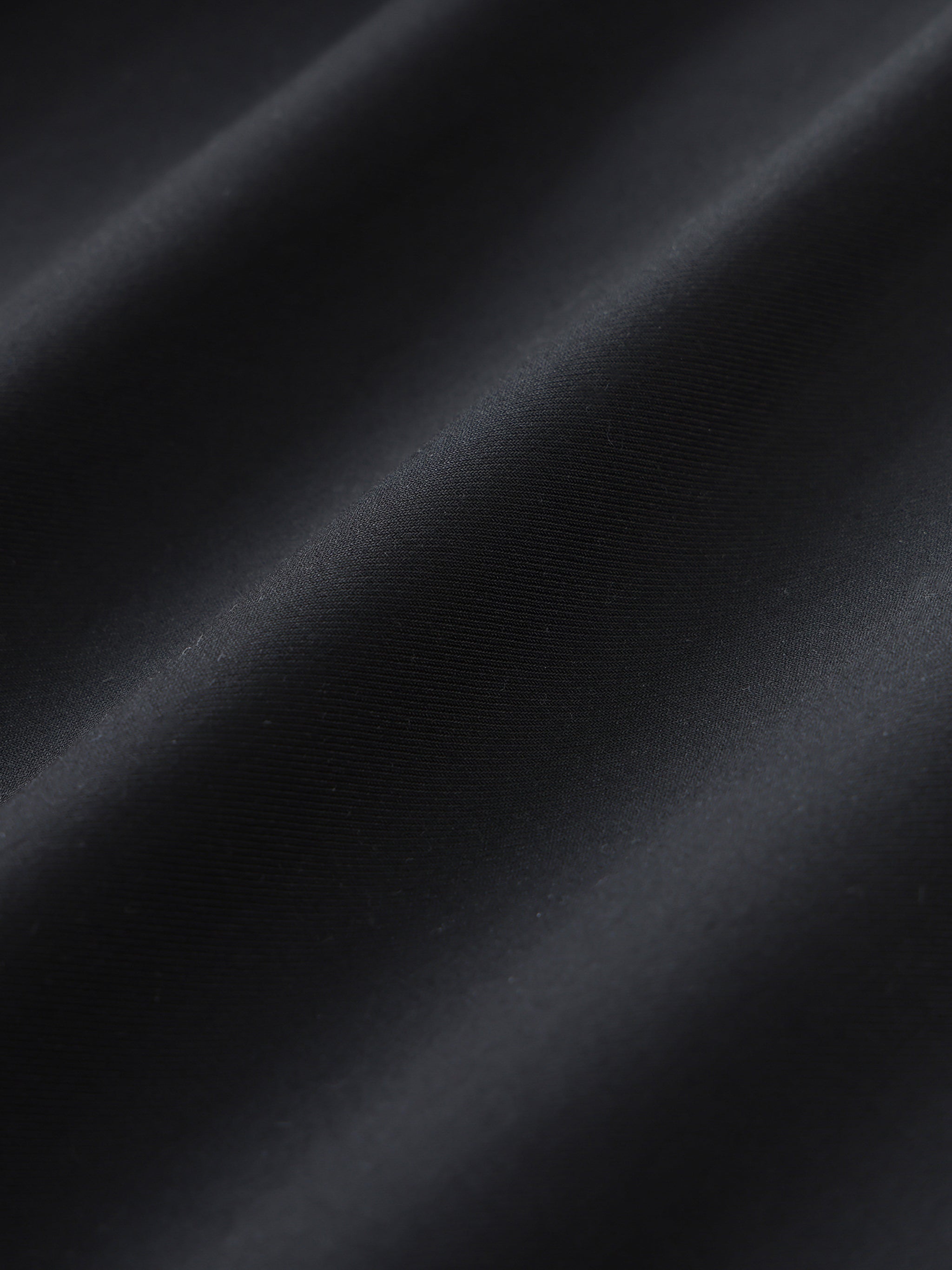 Close-up of smooth black dress pants fabric with soft diagonal folds