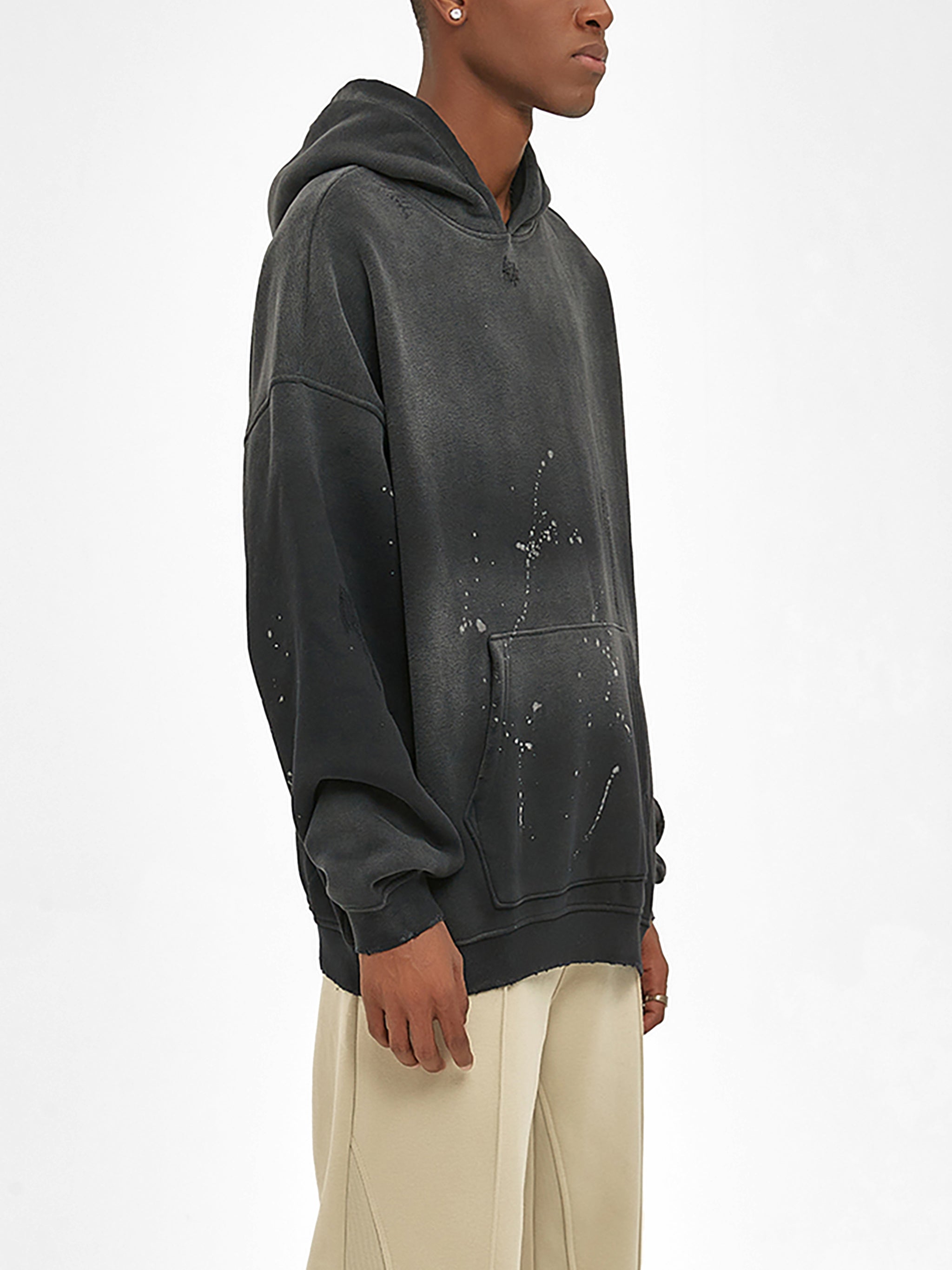 Man wearing a black oversized hoodie with paint splatter design and beige pants