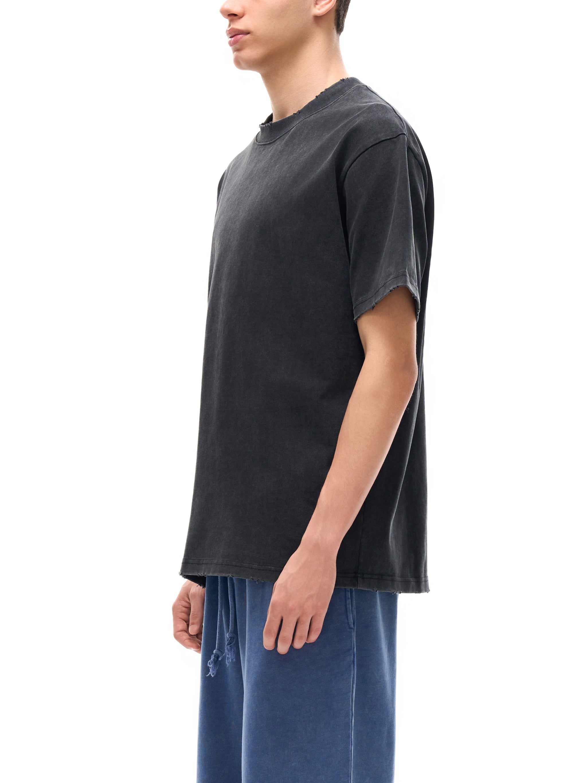 Man wearing oversized black heavyweight t-shirt and blue streetwear shorts, side view