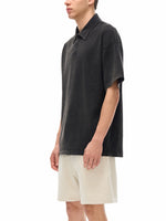 Man wearing a black oversized heavyweight polo shirt and light shorts on white background