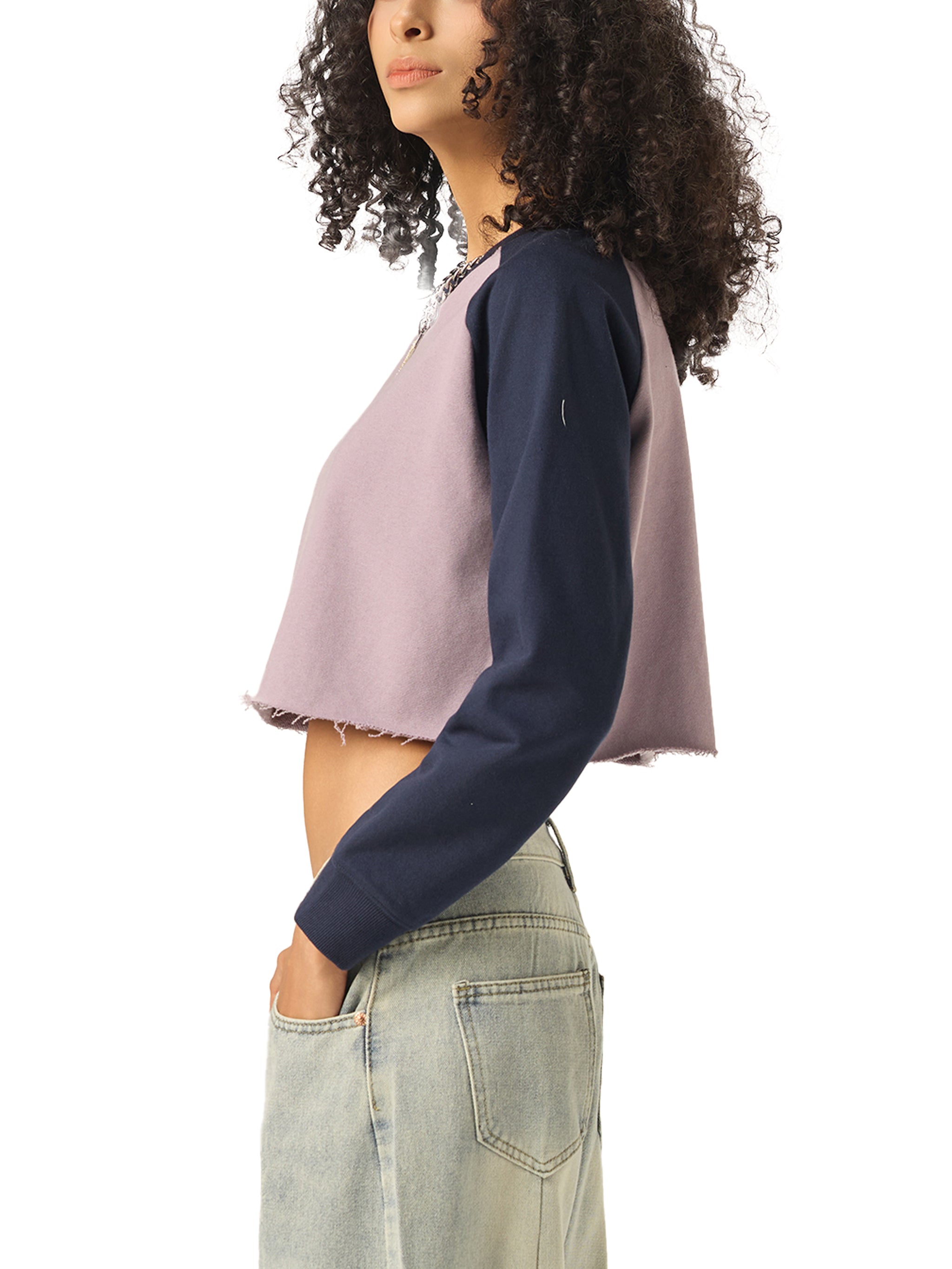 Woman in a cropped two-tone long sleeve top and light wash denim jeans, side view