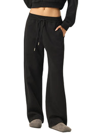 Woman wearing black wide-leg sweatpants with drawstring waist, relaxed streetwear style