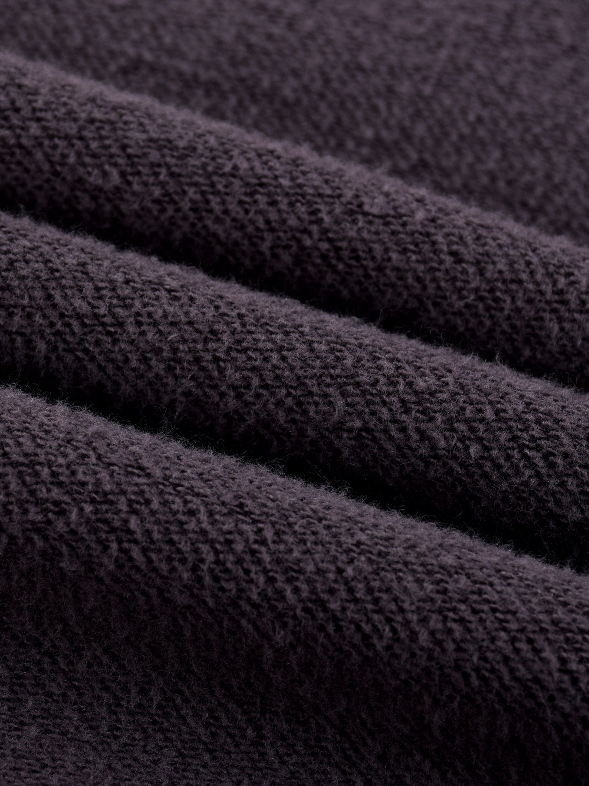 Close-up of heavyweight textured black fleece fabric, soft and cozy material folds
