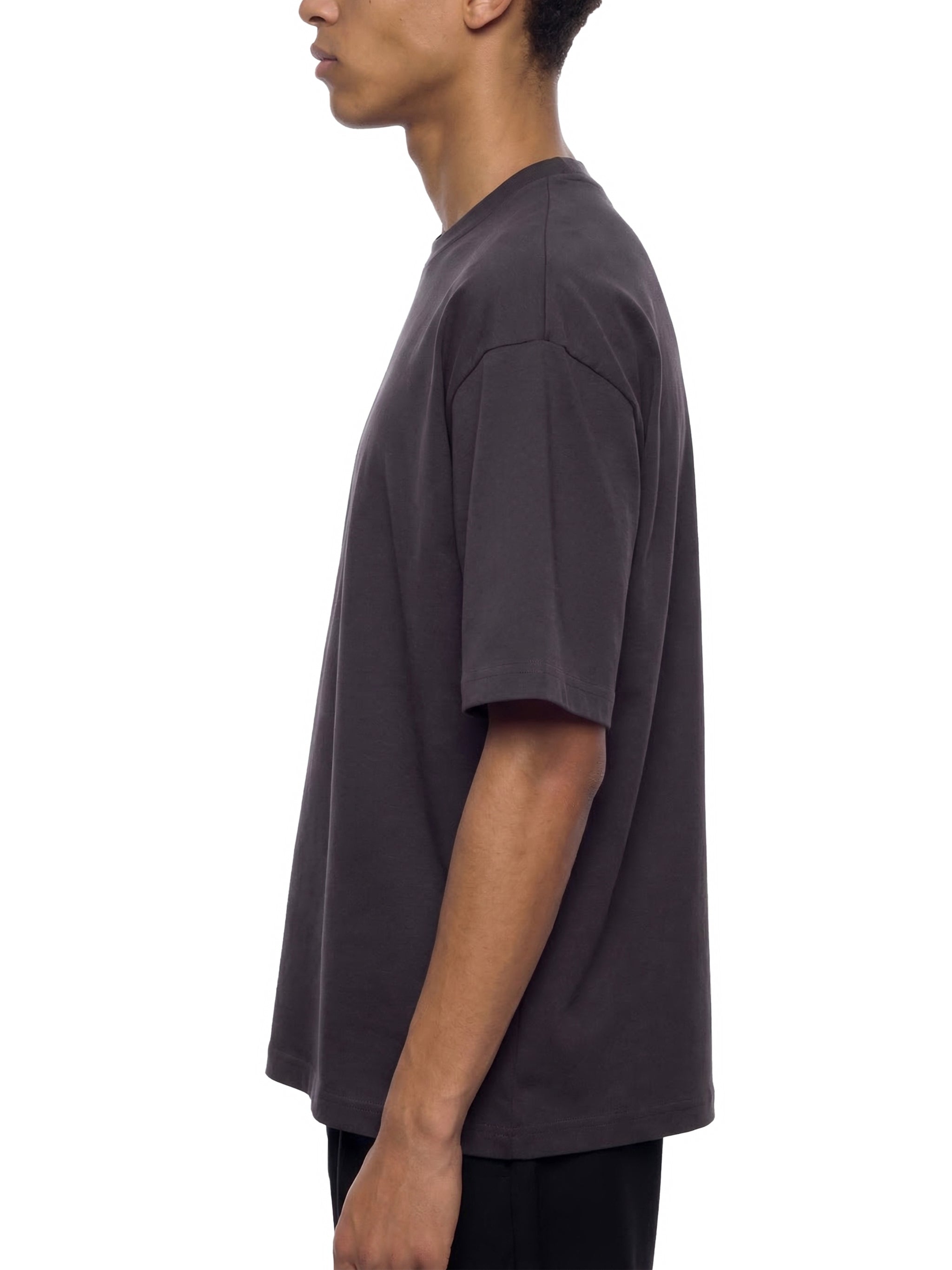 Side view of man in oversized heavyweight black t-shirt and black pants, minimalist style