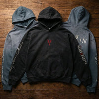 Three heavyweight sunfade oversized hoodies with graphic text and embroidery on wooden floor.