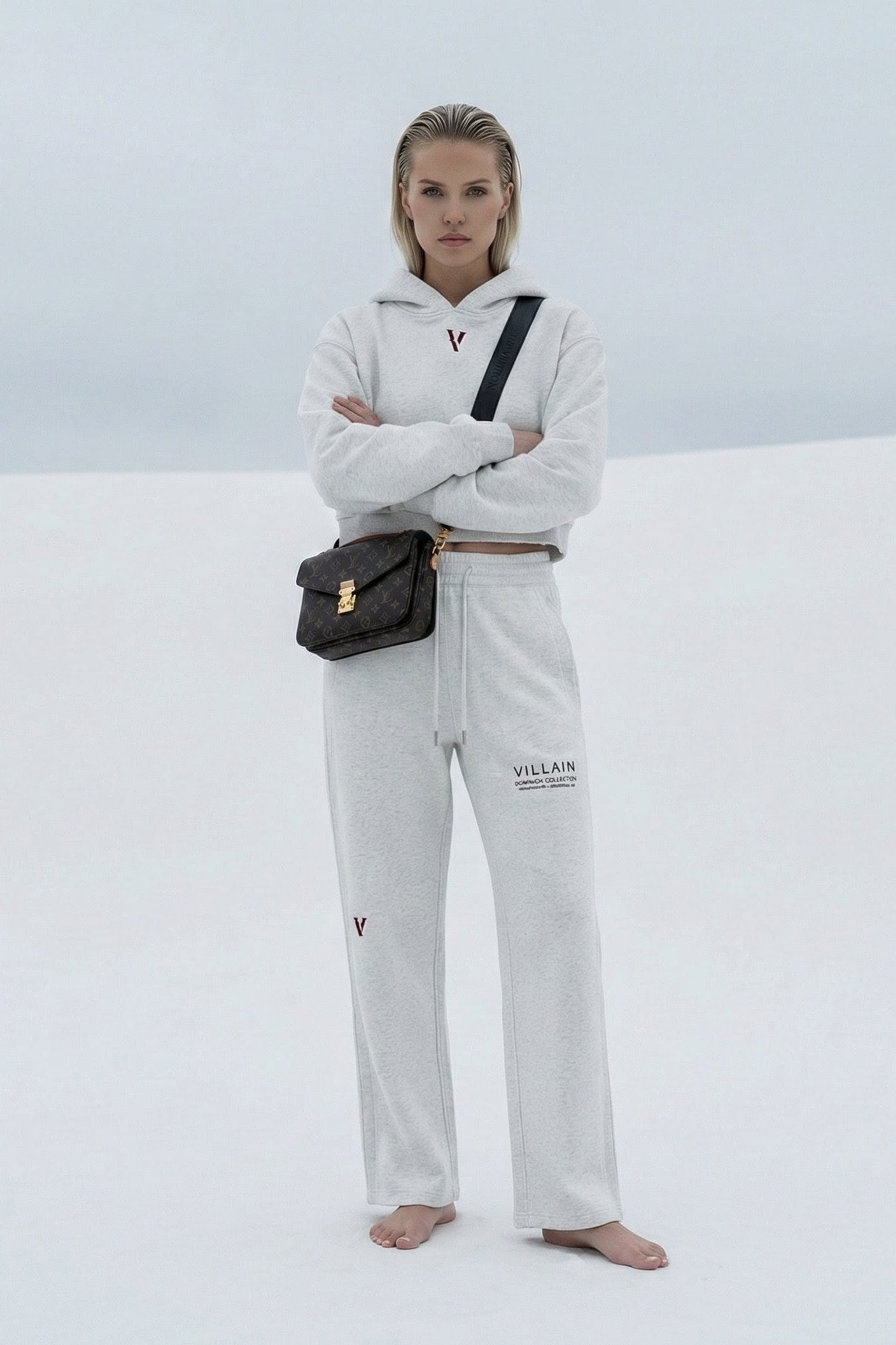 Woman wearing white cropped hoodie and sweatpants with 'Villain' text, standing barefoot outdoors