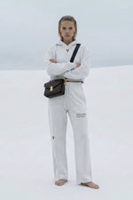 Woman wearing white cropped hoodie and sweatpants with 'Villain' text, standing barefoot outdoors