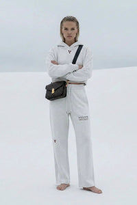 Woman wearing white cropped hoodie and sweatpants with 'Villain' text, standing barefoot outdoors
