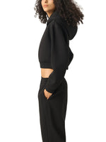 Woman wearing black cropped hoodie and sweatpants, side view, minimal background