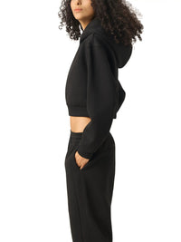 Woman wearing black cropped hoodie and sweatpants, side view, minimal background