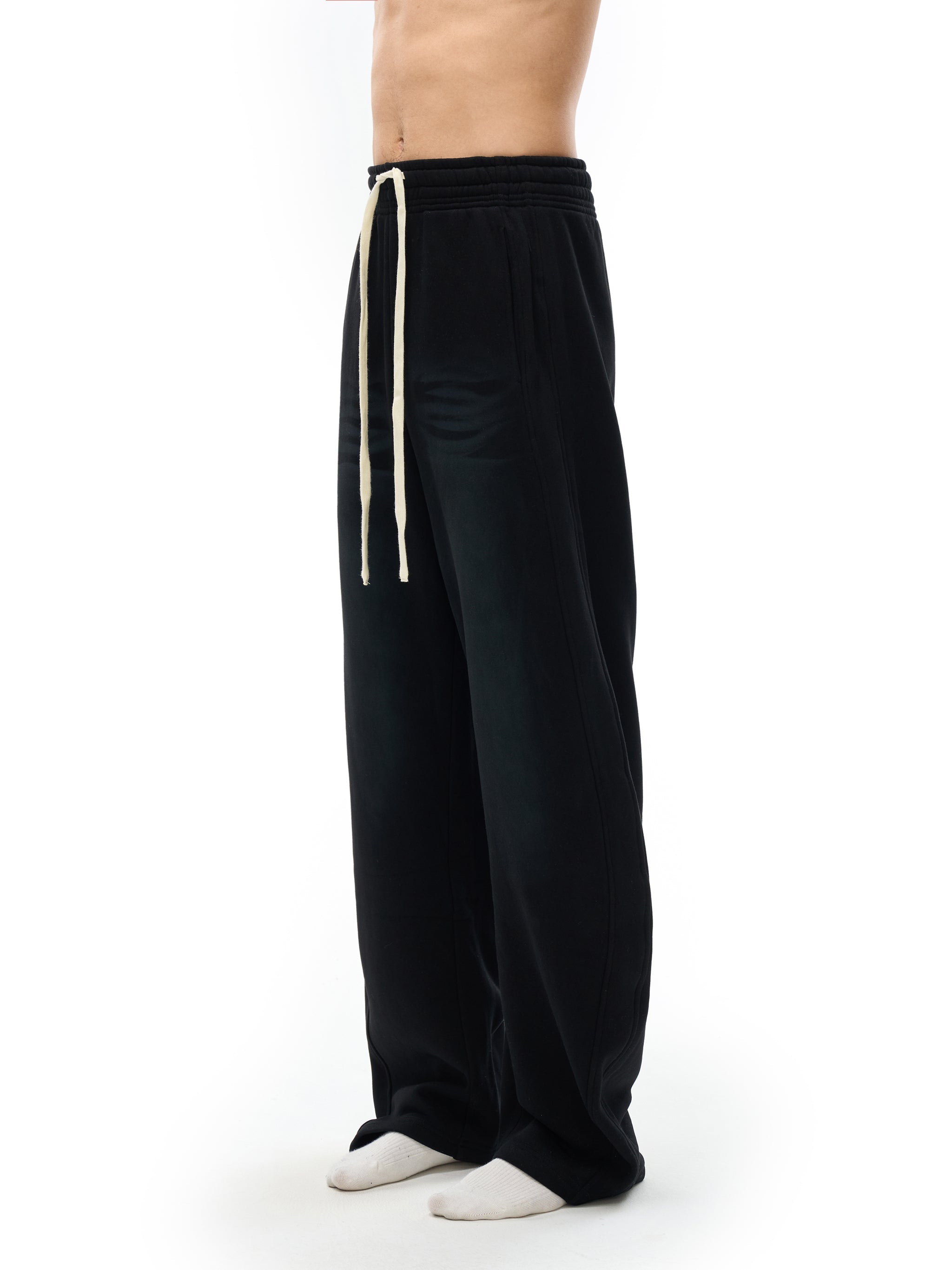 Black fleece sweatpants with wide leg fit and cream drawstring on model standing sideways