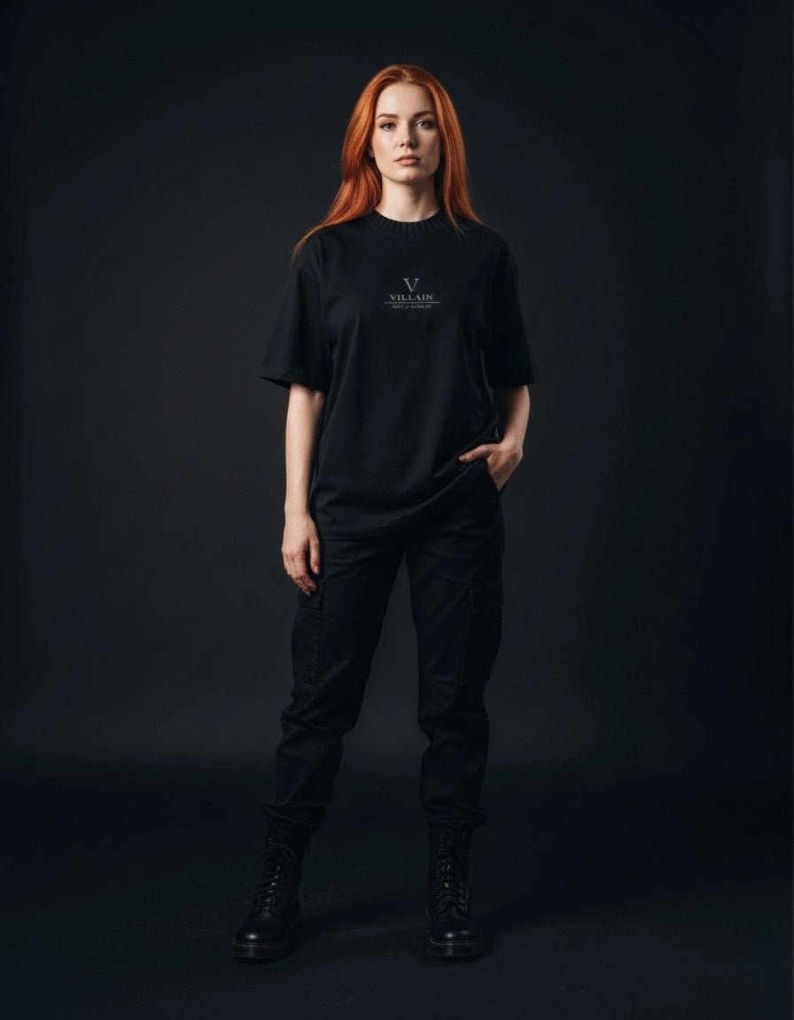 Woman wearing a black heavyweight knitted round neck t-shirt with 'Villain' text, black pants, and boots, posing against a dark background.
