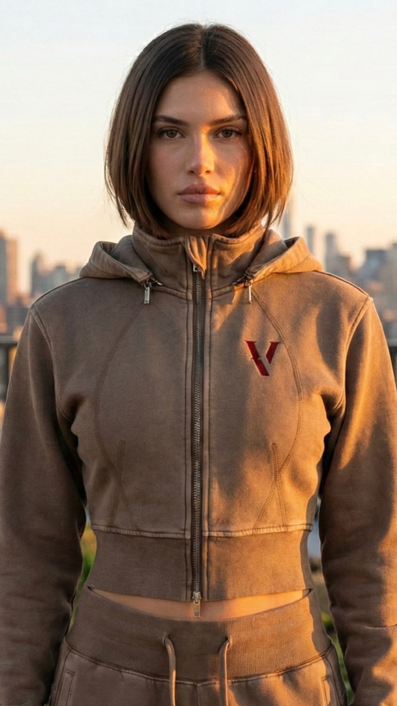 Woman wearing brown vintage-washed cropped fleece hoodie with front zip and red V logo outdoors