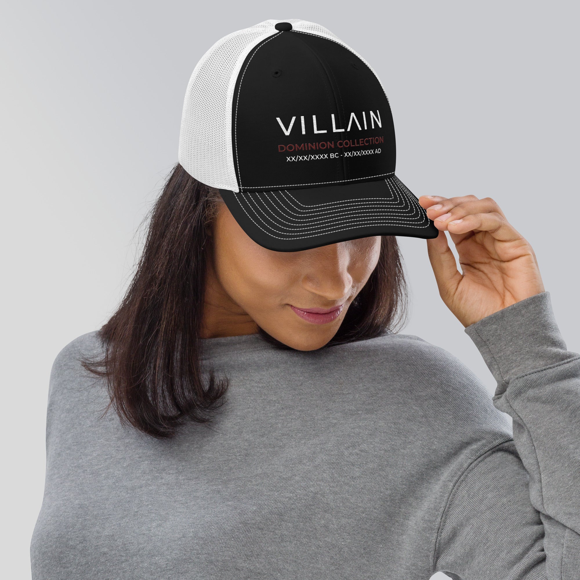 Woman wearing black and white trucker cap with 'VILLAIN Dominion Collection' text, modern streetwear style