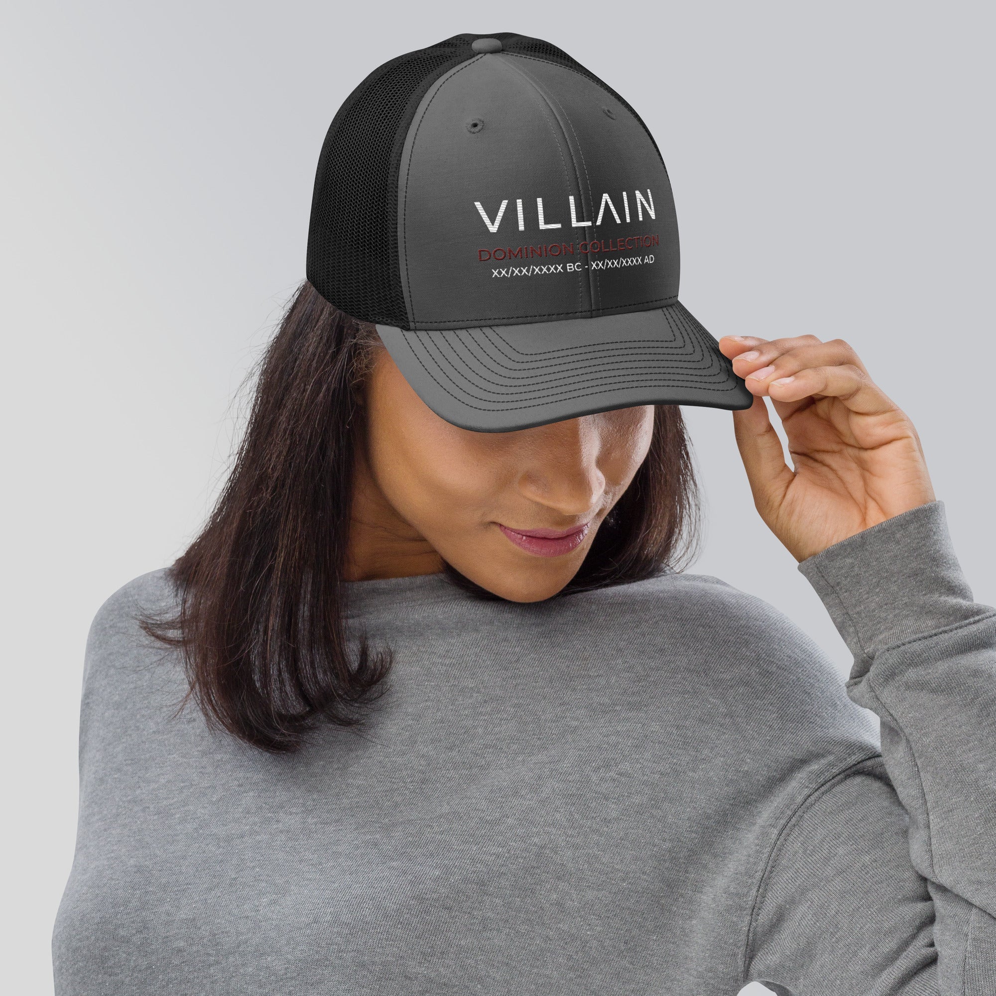 Woman wearing black mesh trucker cap with 'VILLAIN Dominion Collection' embroidered text.