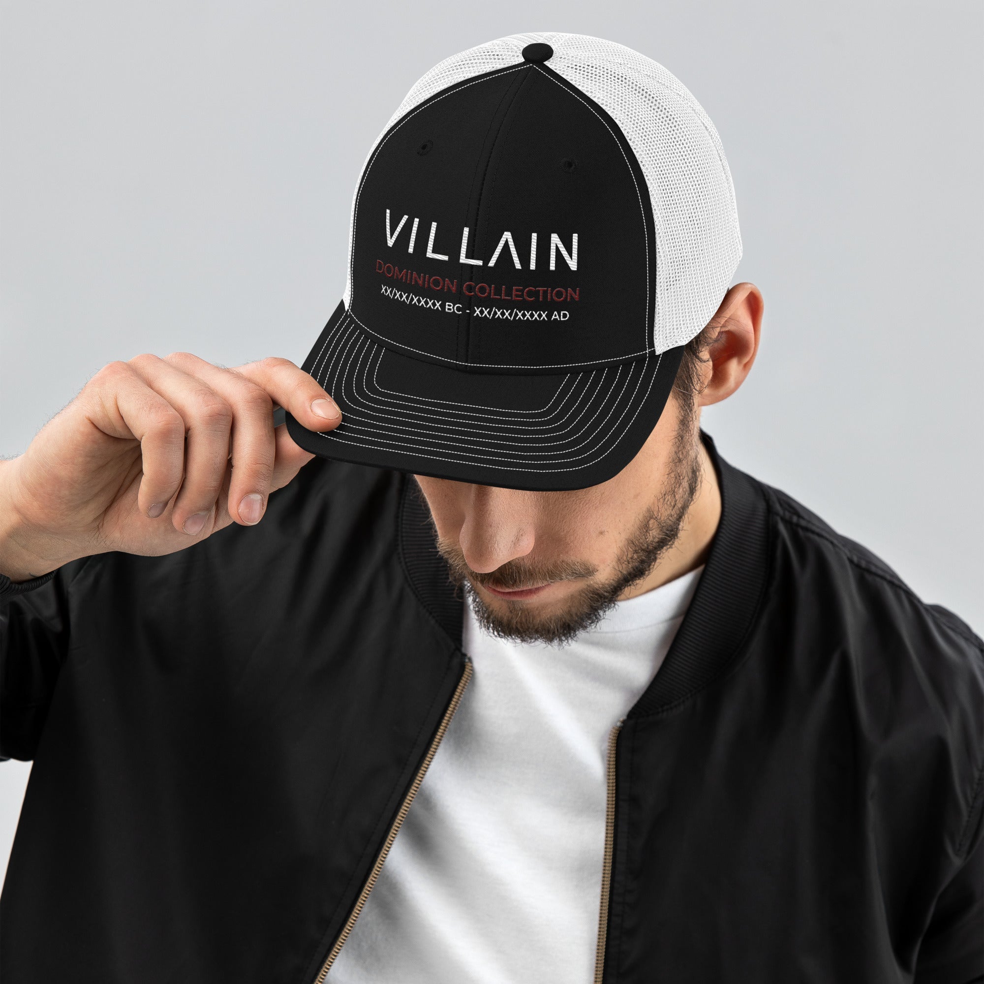 Man wearing black and white trucker cap with 'VILLAIN Dominion Collection' text, streetwear style