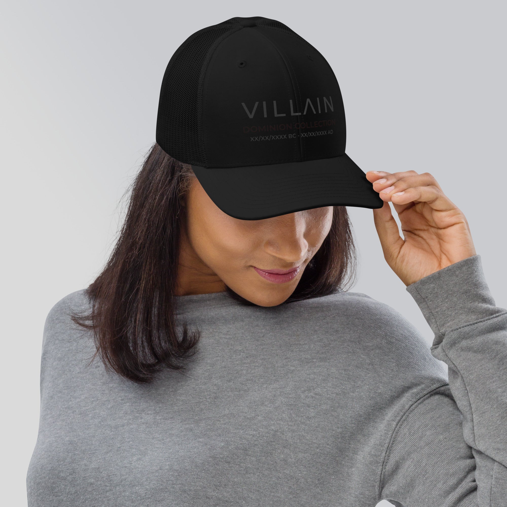 Woman wearing black trucker cap with 'VILLAIN Dominion Collection' text, casual streetwear style