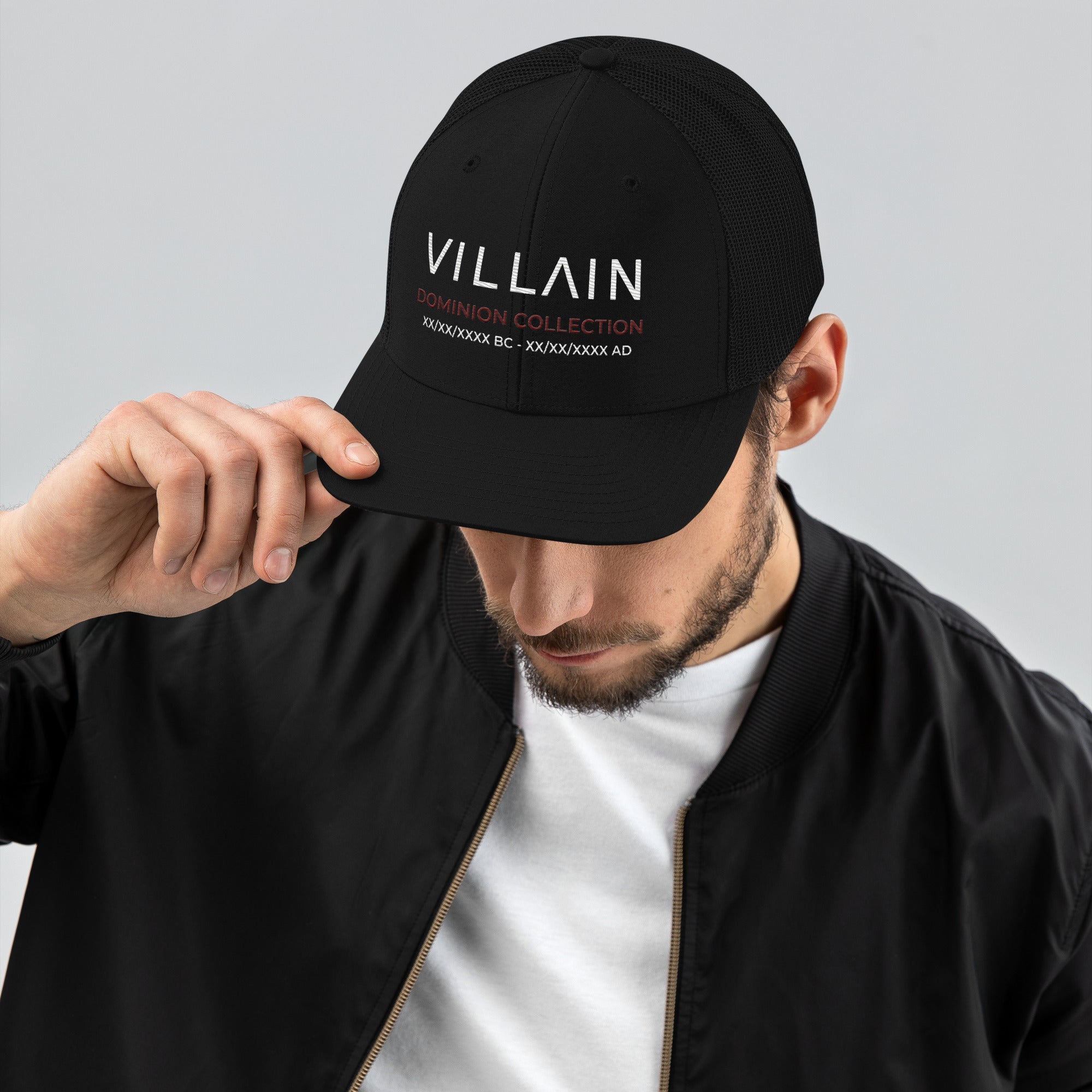 Man wearing black trucker cap with 'VILLAIN Dominion Collection' text, streetwear style