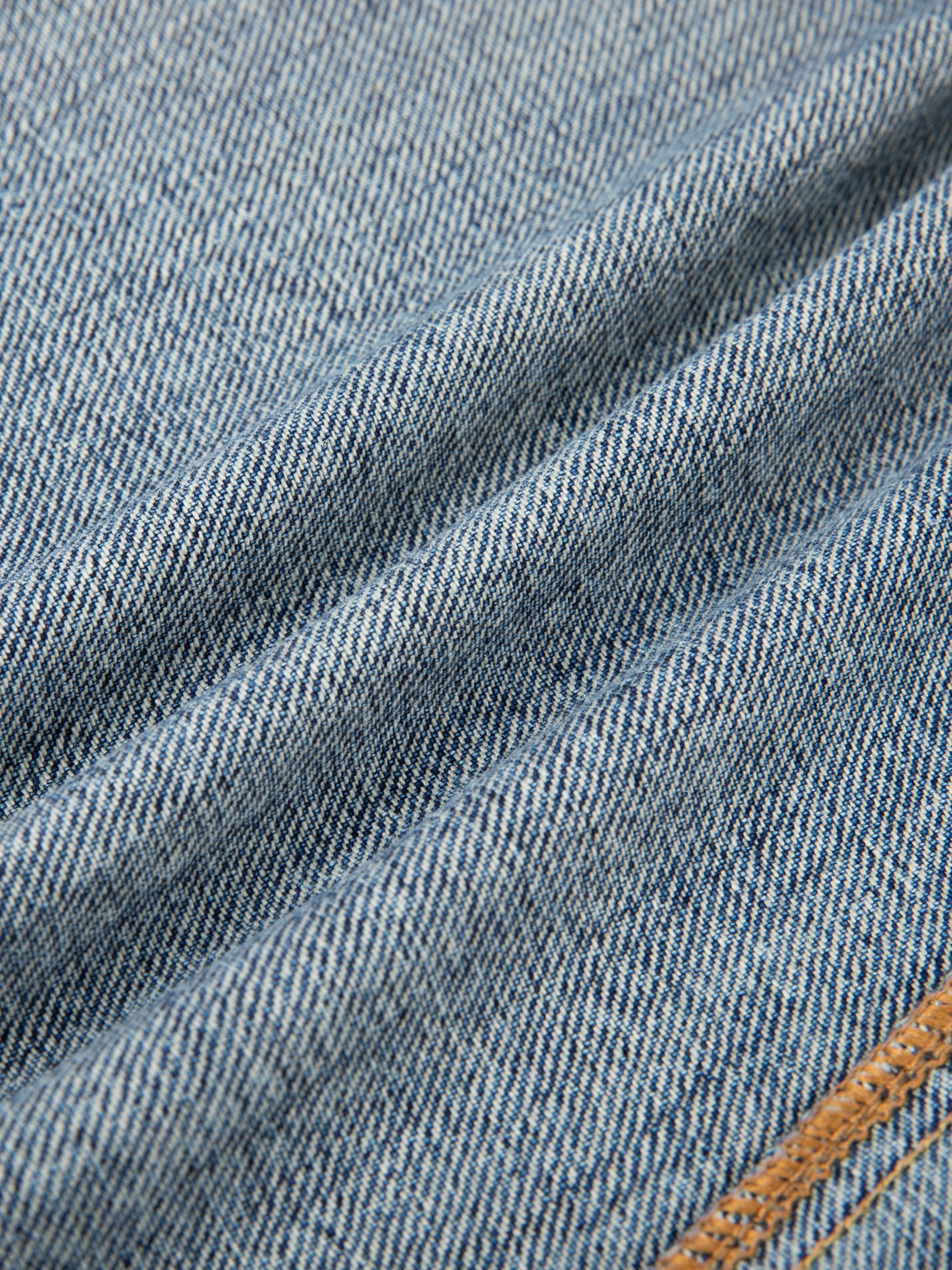 Close-up of vintage wash baggy denim jeans fabric with visible seam and blue texture