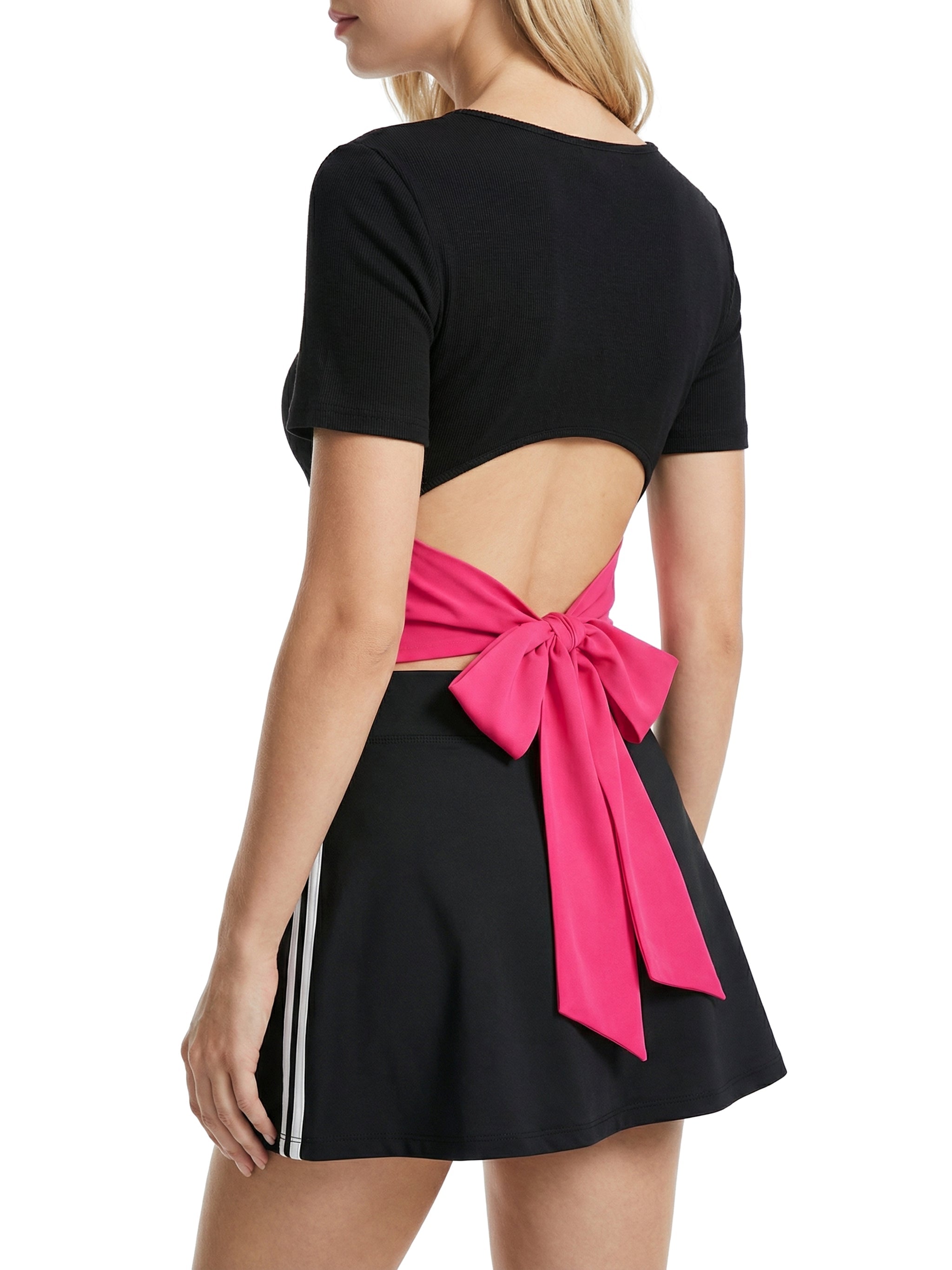 Woman wearing black short sleeve open-back top with large pink bow and black mini skirt