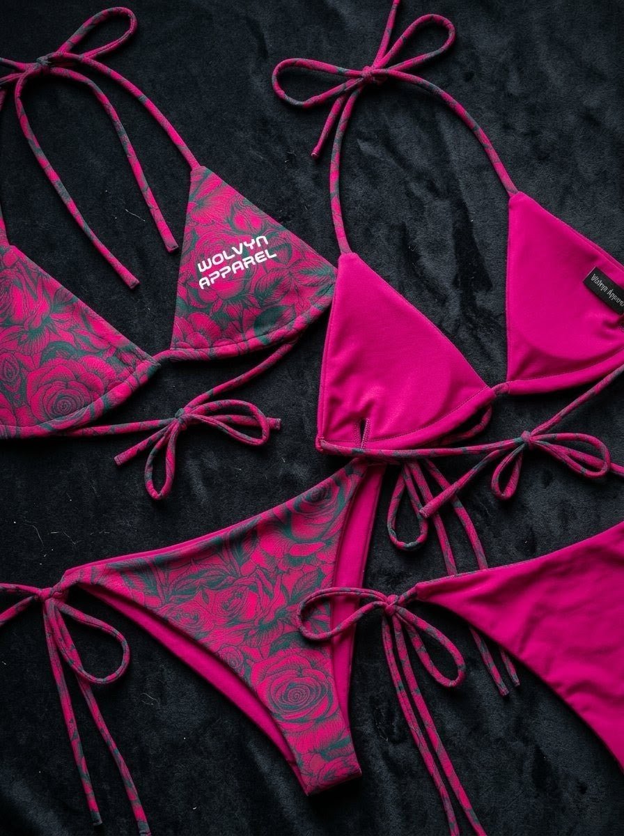 Pink and black floral string bikini set with tie sides and halter neck, laid on black fabric.