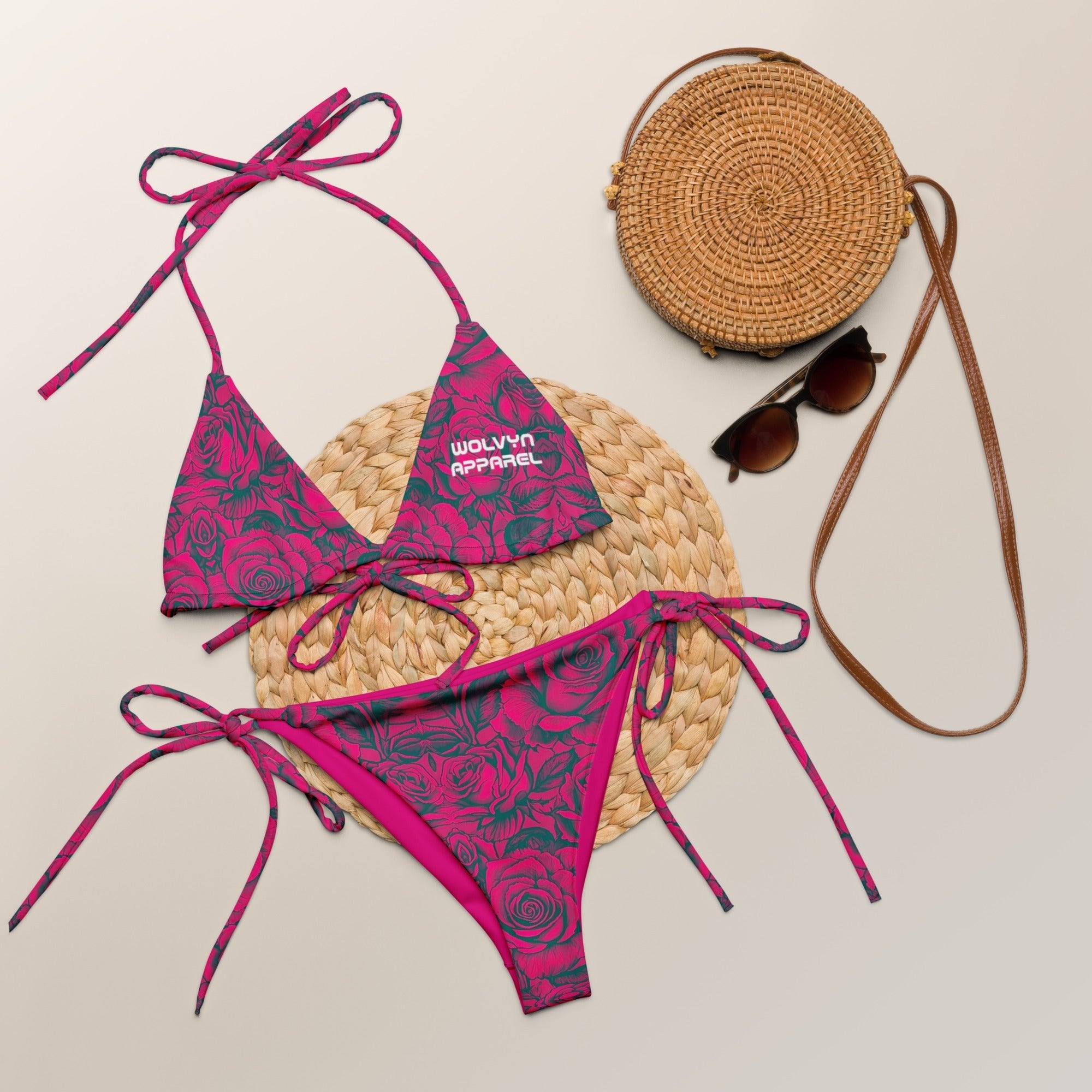 Pink floral string bikini with rose pattern, straw bag, and sunglasses on neutral background