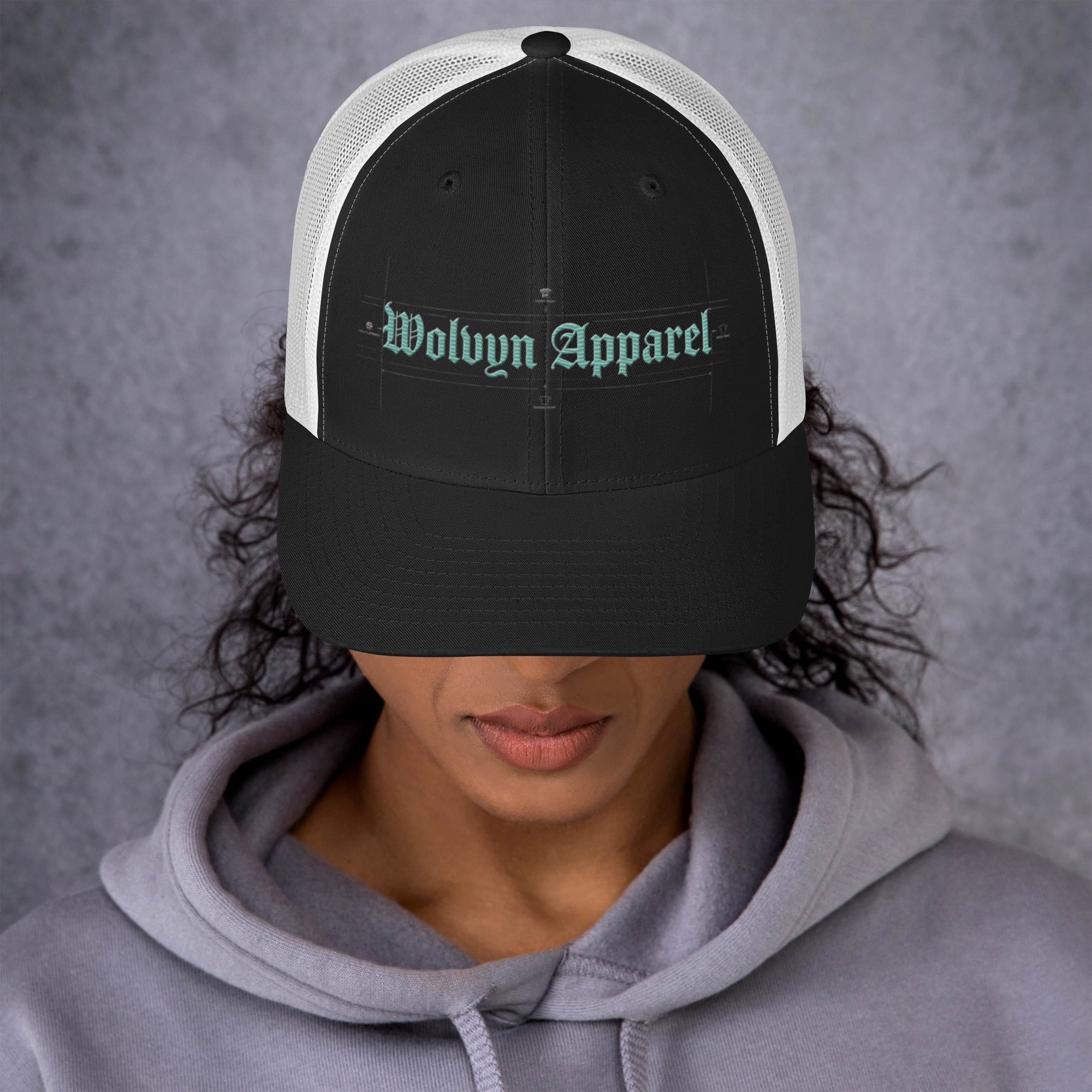 Woman wearing a black and white mid-profile trucker cap with embroidered Wolvyn Apparel text