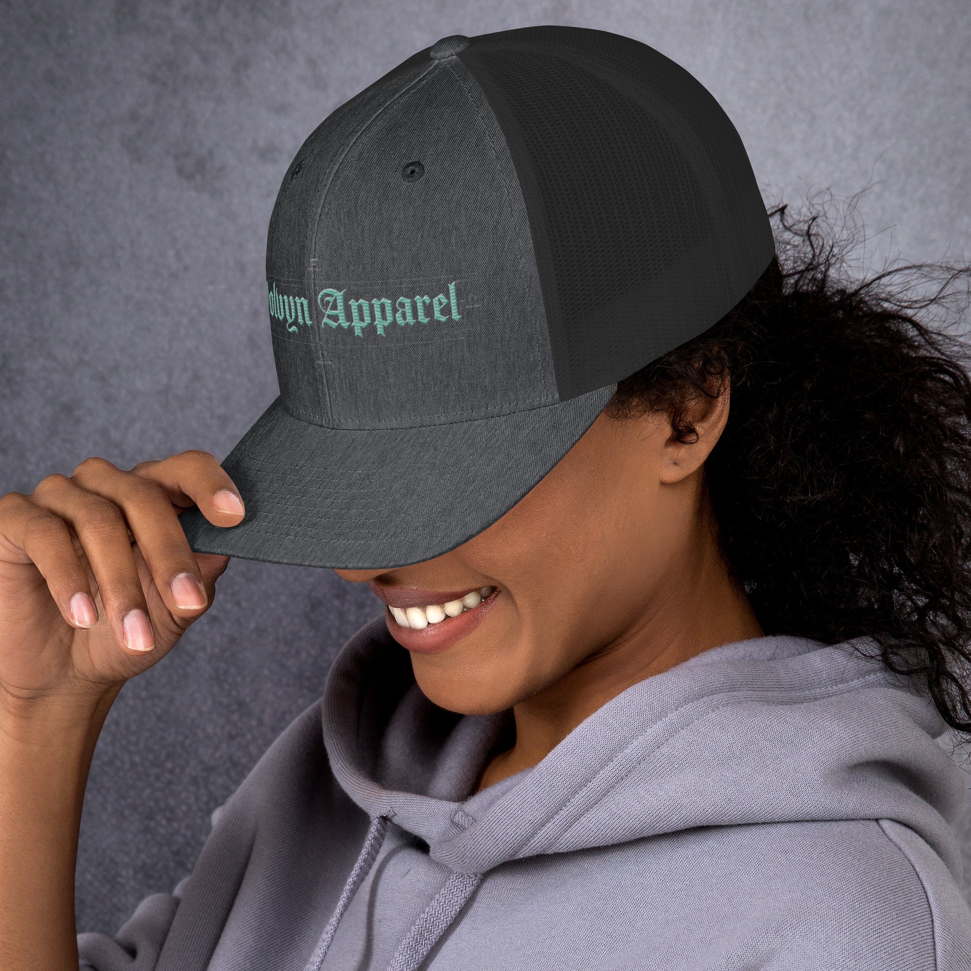 Charcoal mid-profile embroidered trucker cap with mesh back worn by woman in gray hoodie