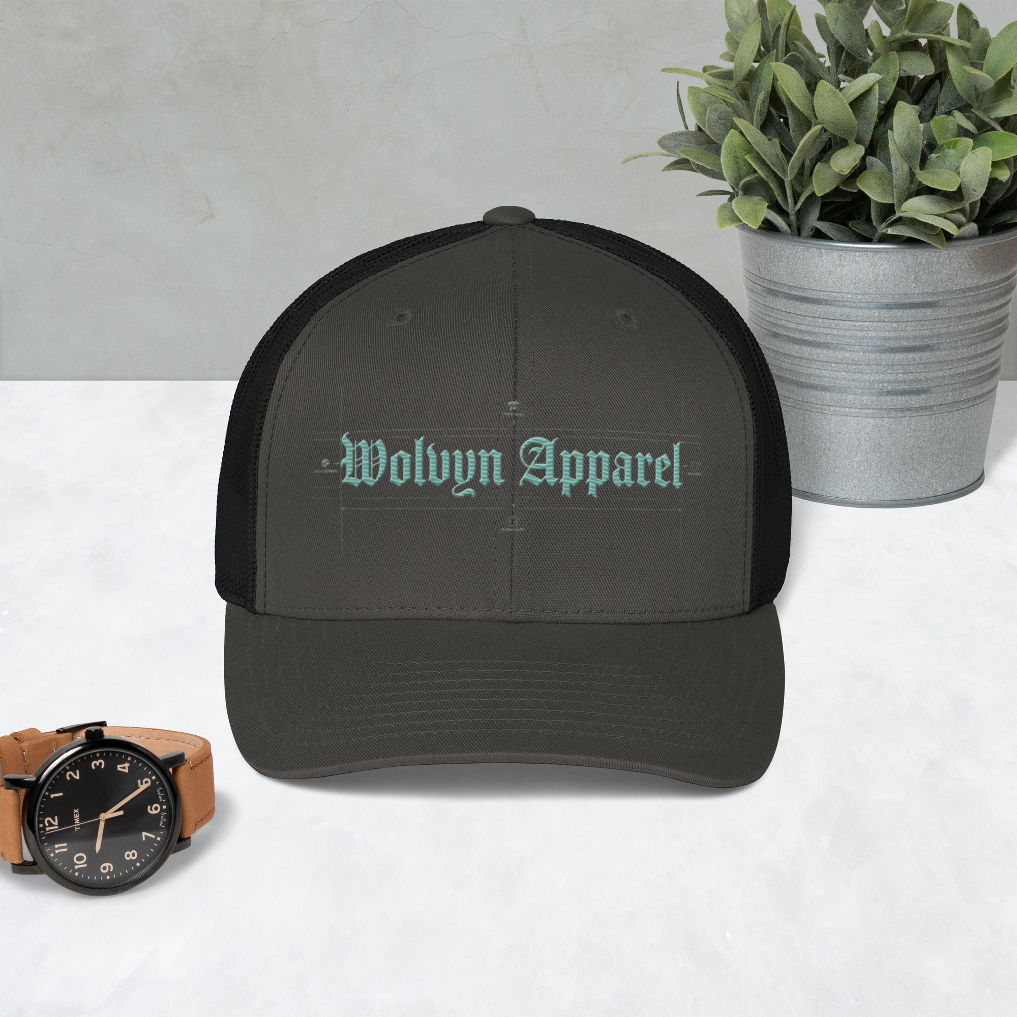 Mid-profile black trucker cap with 'Wolvyn Apparel' embroidered on front, on table.