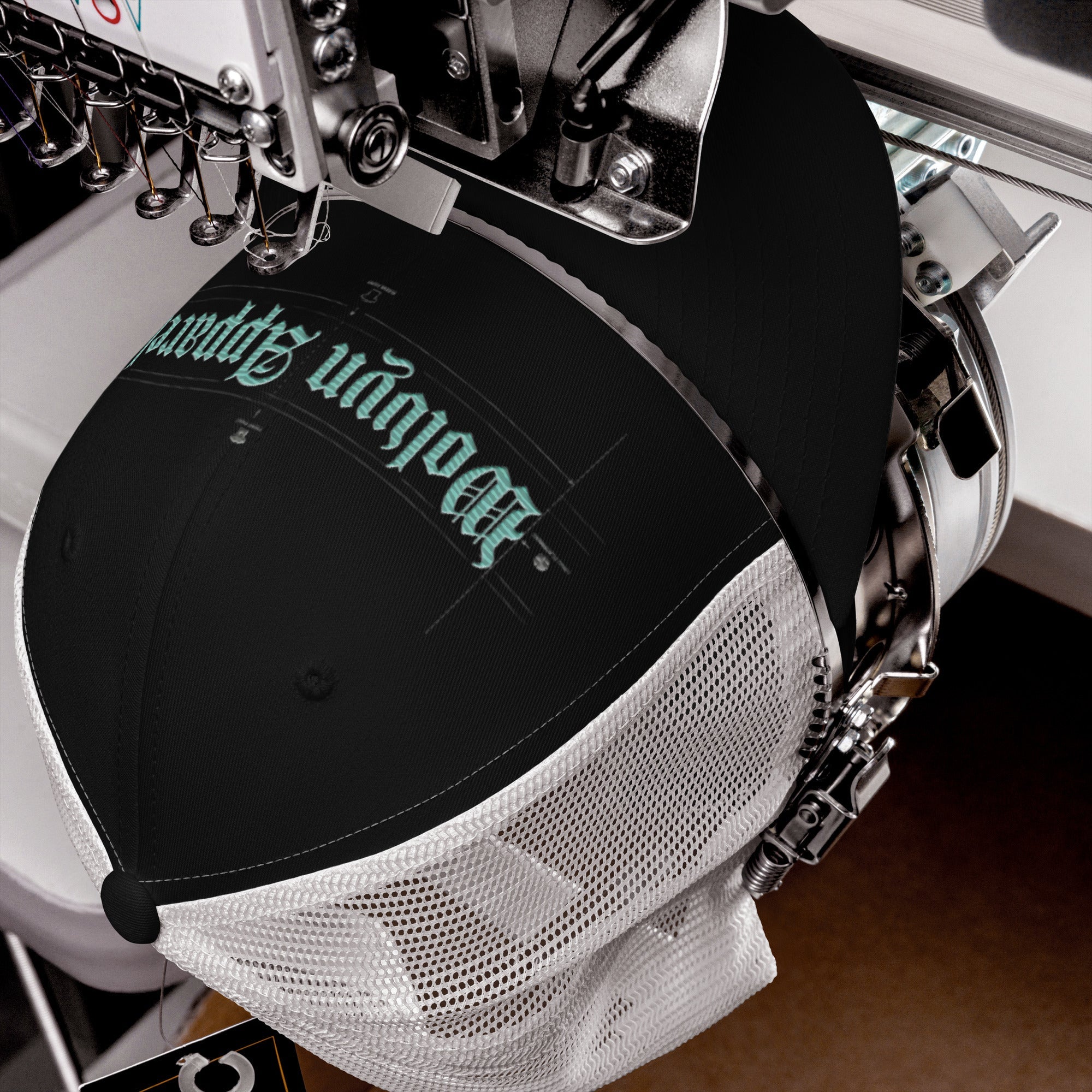 Black and white trucker cap with blue embroidered text being stitched by embroidery machine