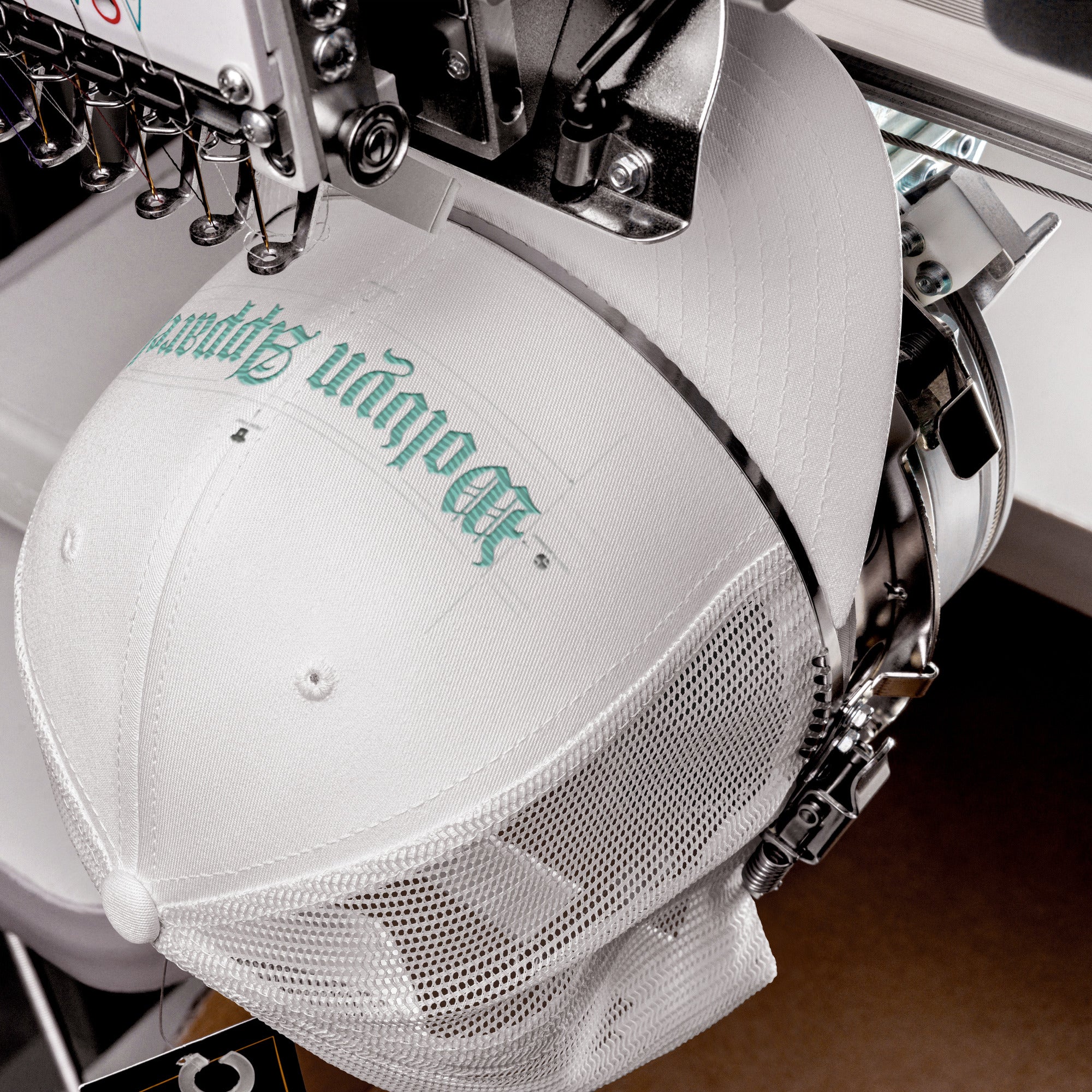 White mid-profile mesh trucker cap with teal embroidery on embroidery machine