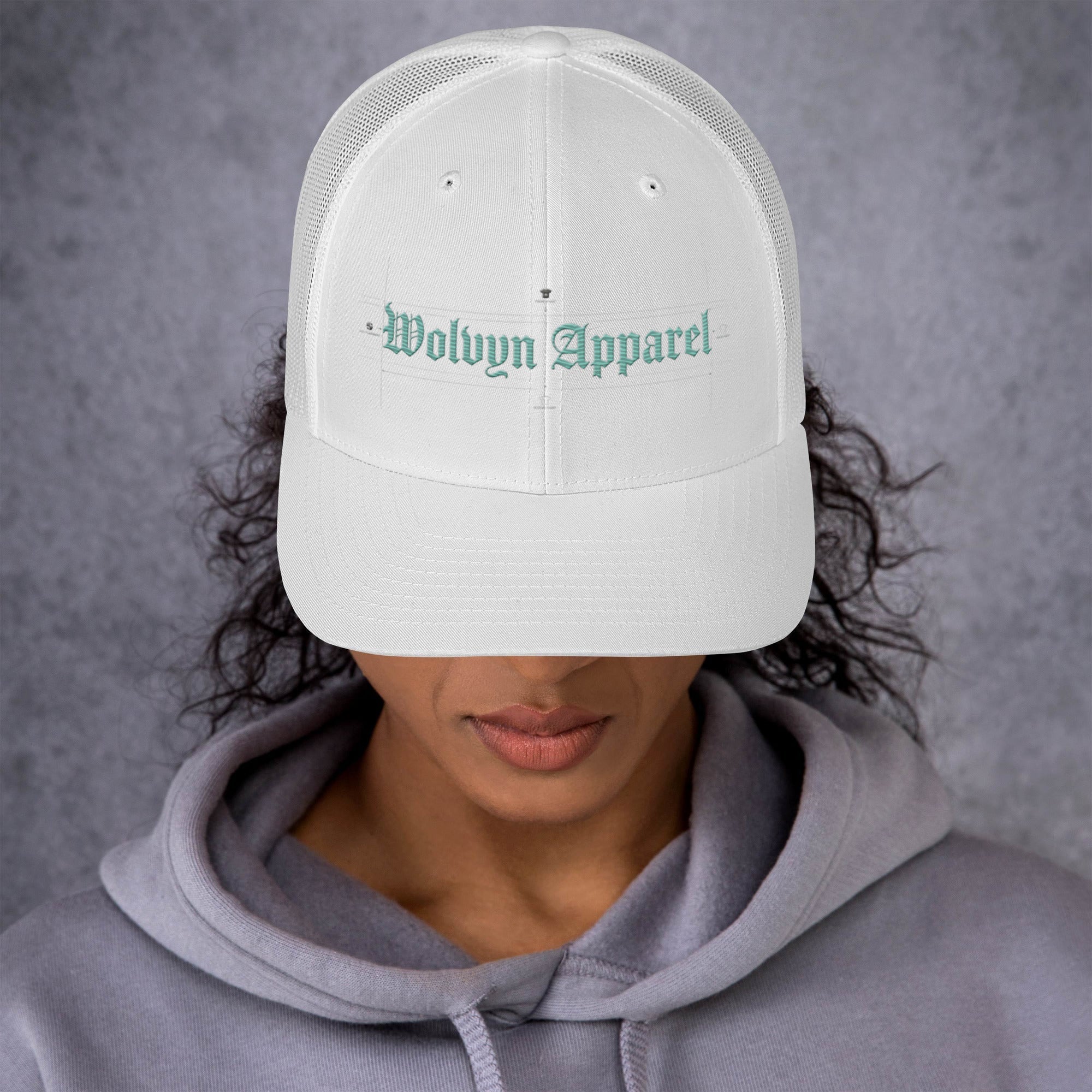 White mid-profile trucker cap with embroidered 'Wolvyn Apparel' text, worn by person in hoodie
