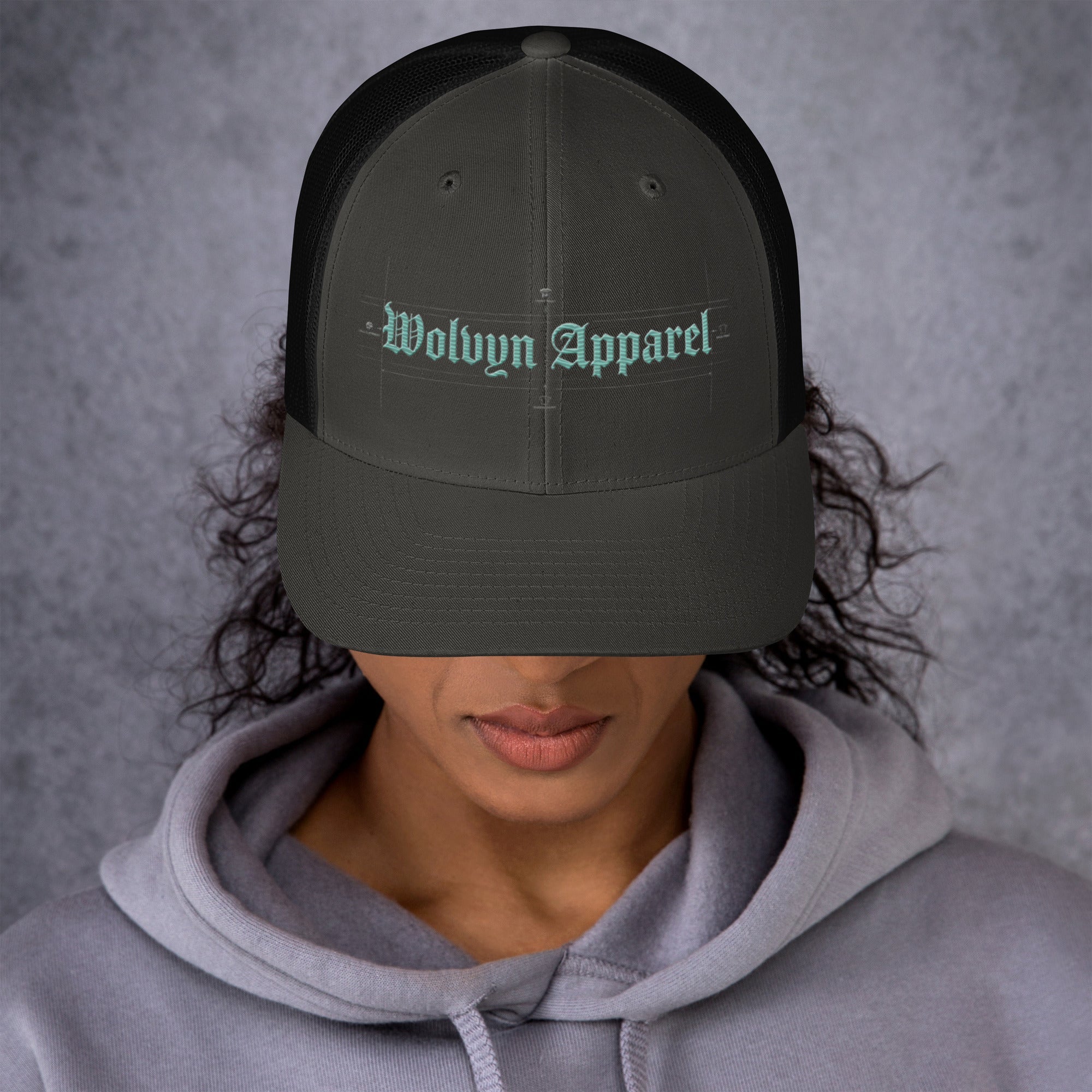 Black mid-profile embroidered trucker cap with 'Wolvyn Apparel' text, worn by woman in hoodie
