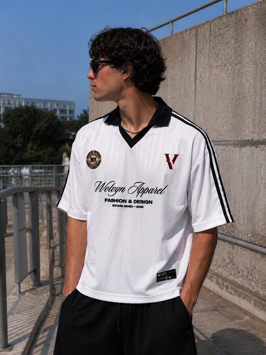 Man in sunglasses wearing a white streetwear shirt with black stripes and bold text outdoors