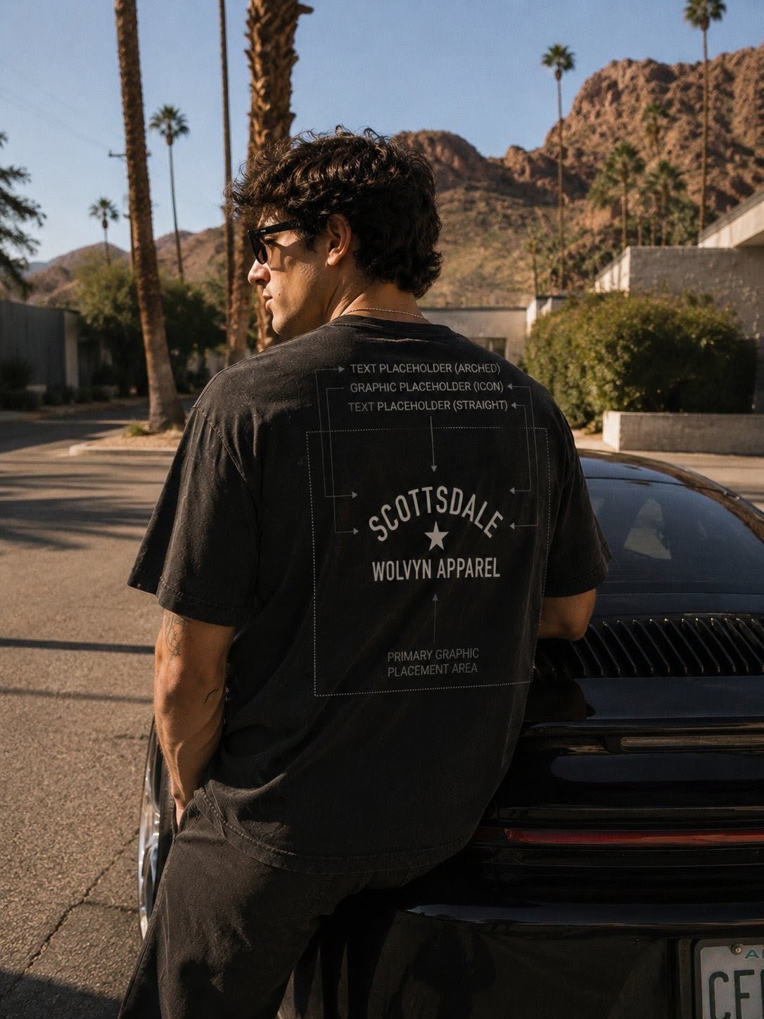 Man in black vintage washed t-shirt with Scottsdale graphic, leaning on car, desert background