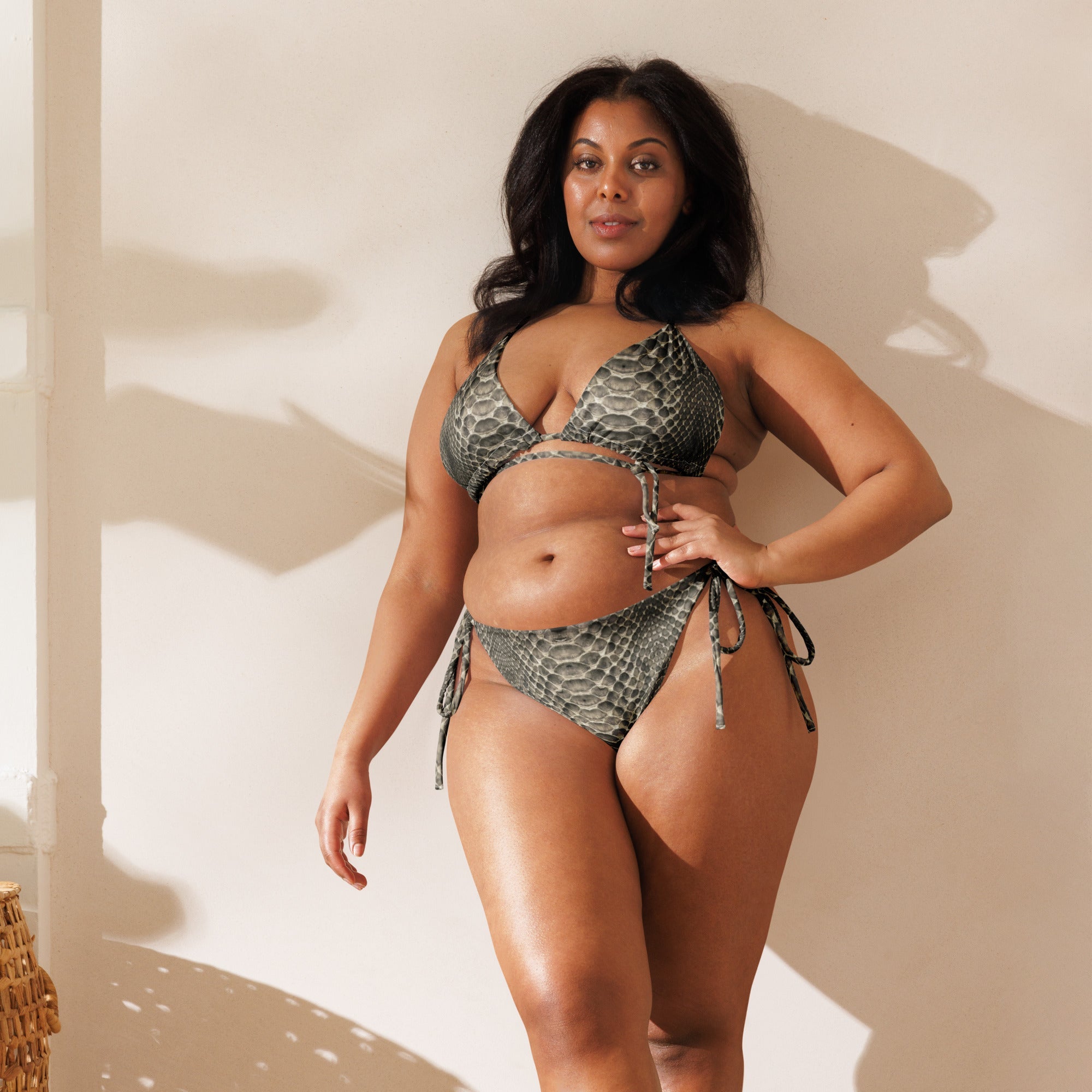 Woman modeling snake print string bikini with wrap detail in sunlit indoor setting.
