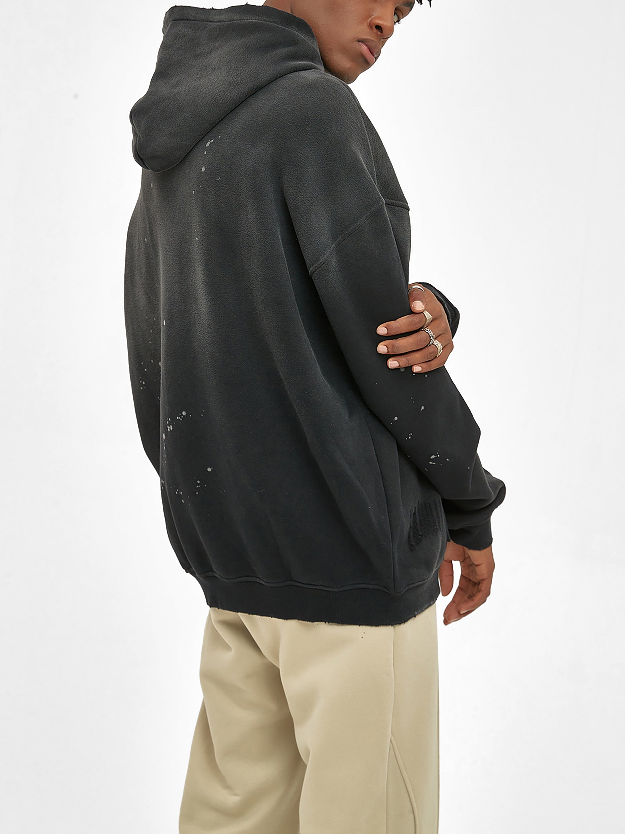 Man wearing a black distressed fleece hoodie with frayed details and beige pants