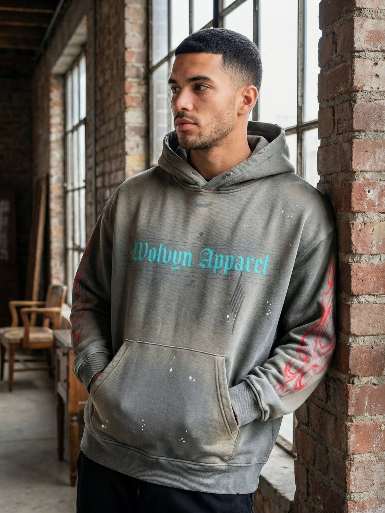 Man wearing frayed fleece hoodie with weathered look, graffiti sleeves, and front pocket indoors