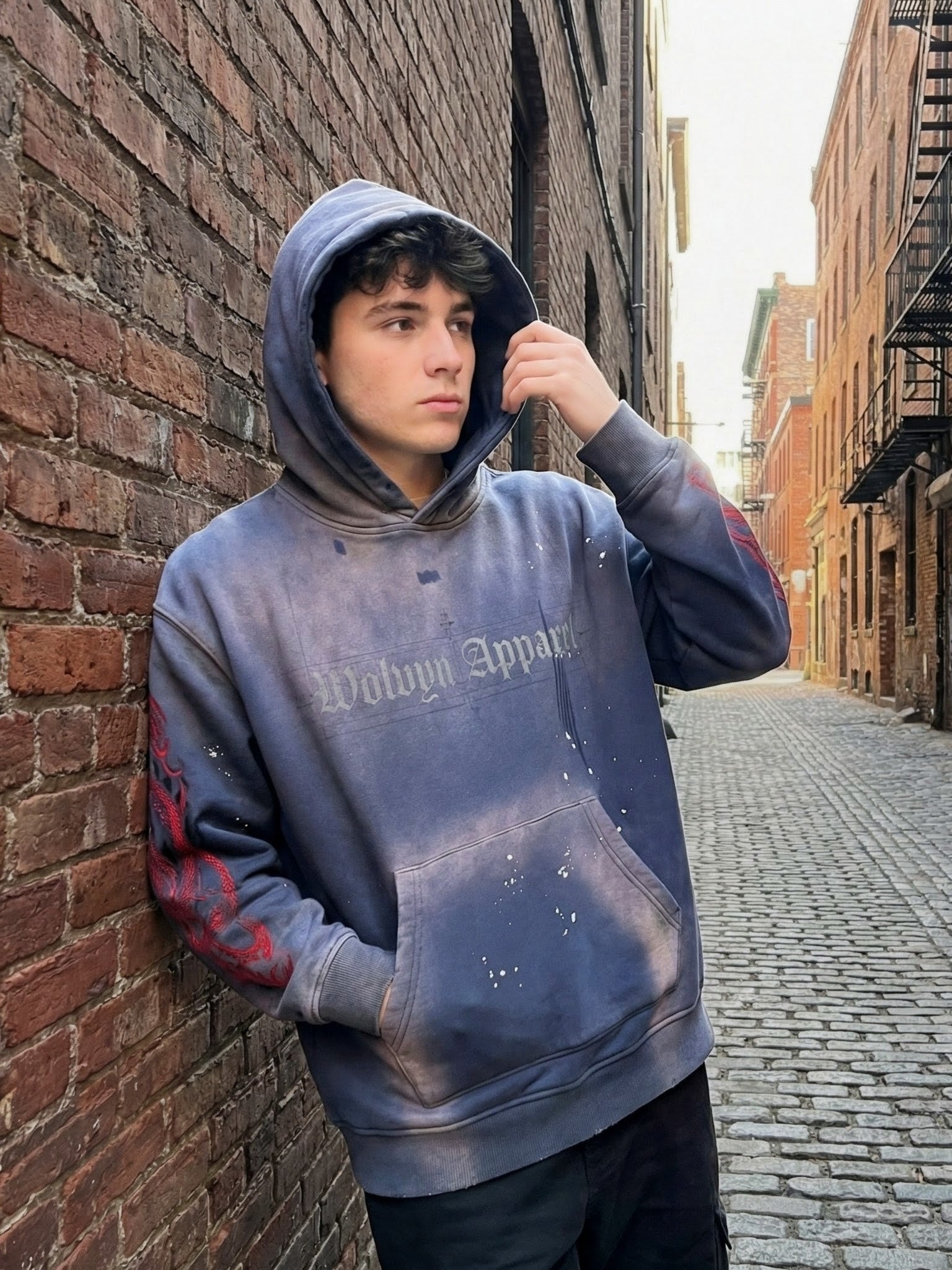 Man wearing weathered fleece hoodie with frayed details and graphic print in urban alley