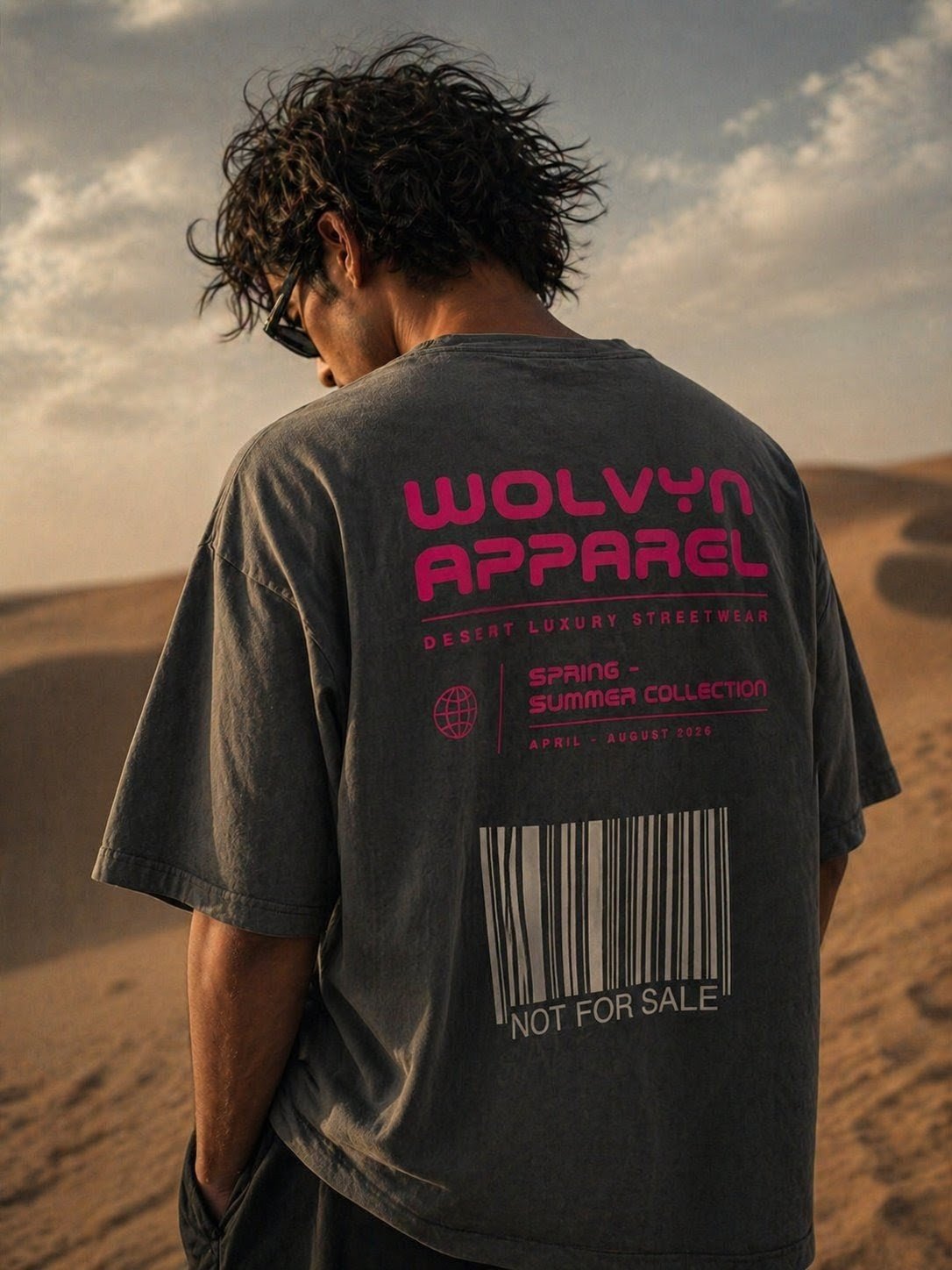 Man wearing oversized black t-shirt with bold pink text and barcode design in desert