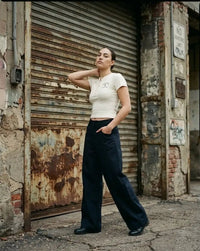 Woman wearing wide-leg black dress pants and a fitted beige top in an urban street setting.