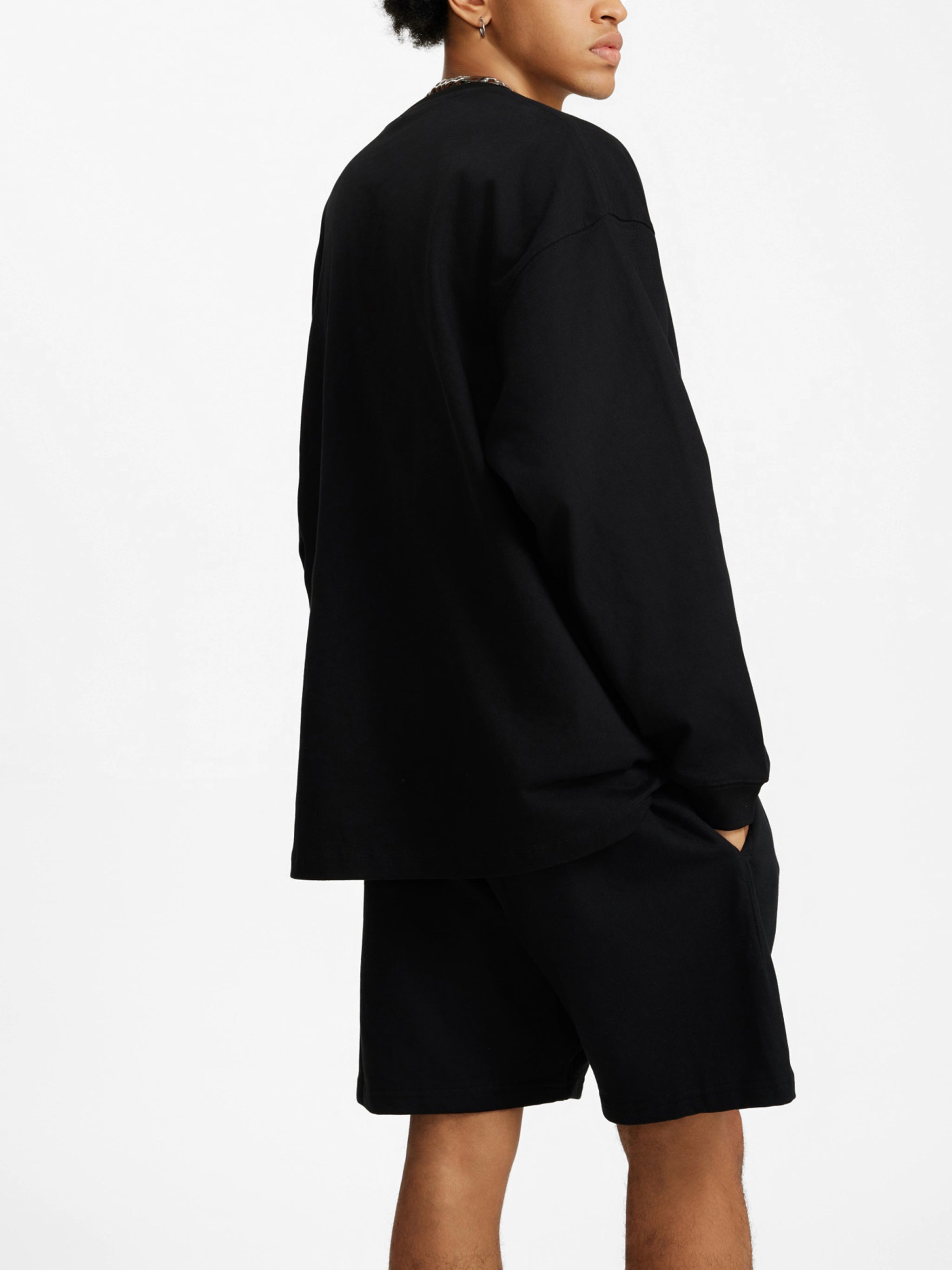 Oversized unisex black long sleeve t-shirt with shorts, model side pose, minimalist streetwear