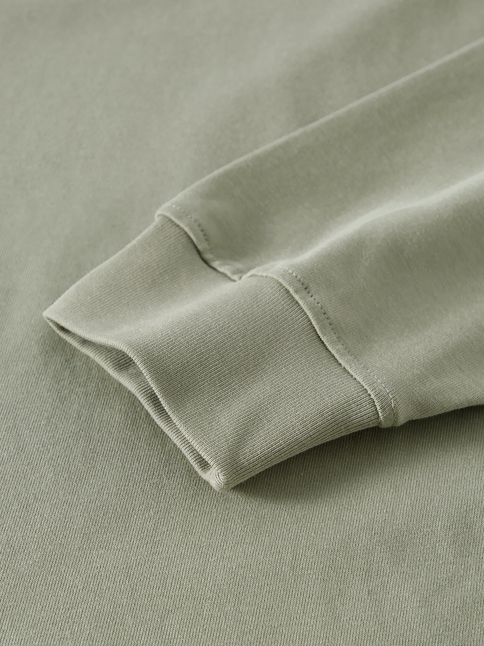 Oversized unisex sage green long sleeve t-shirt with close-up of sleeve cuff